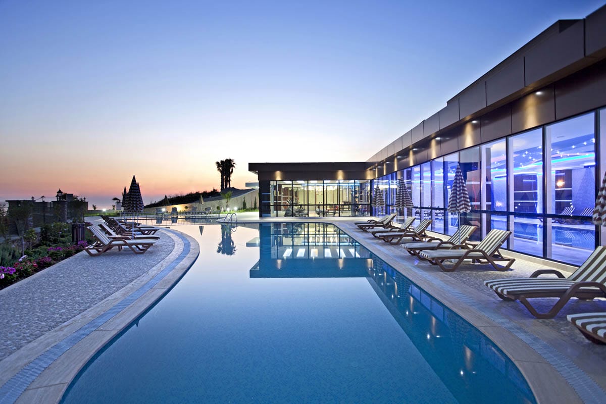 Long outdoor pool with wooden loungers and palms for residents of villas in Kargicak