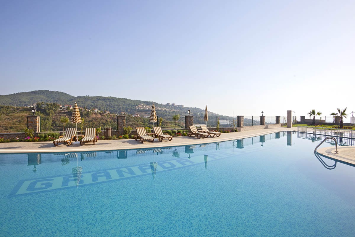 Outdoor pool with striped umbrellas and loungers on the grounds of a villa residence in Kargicak, Turkey
