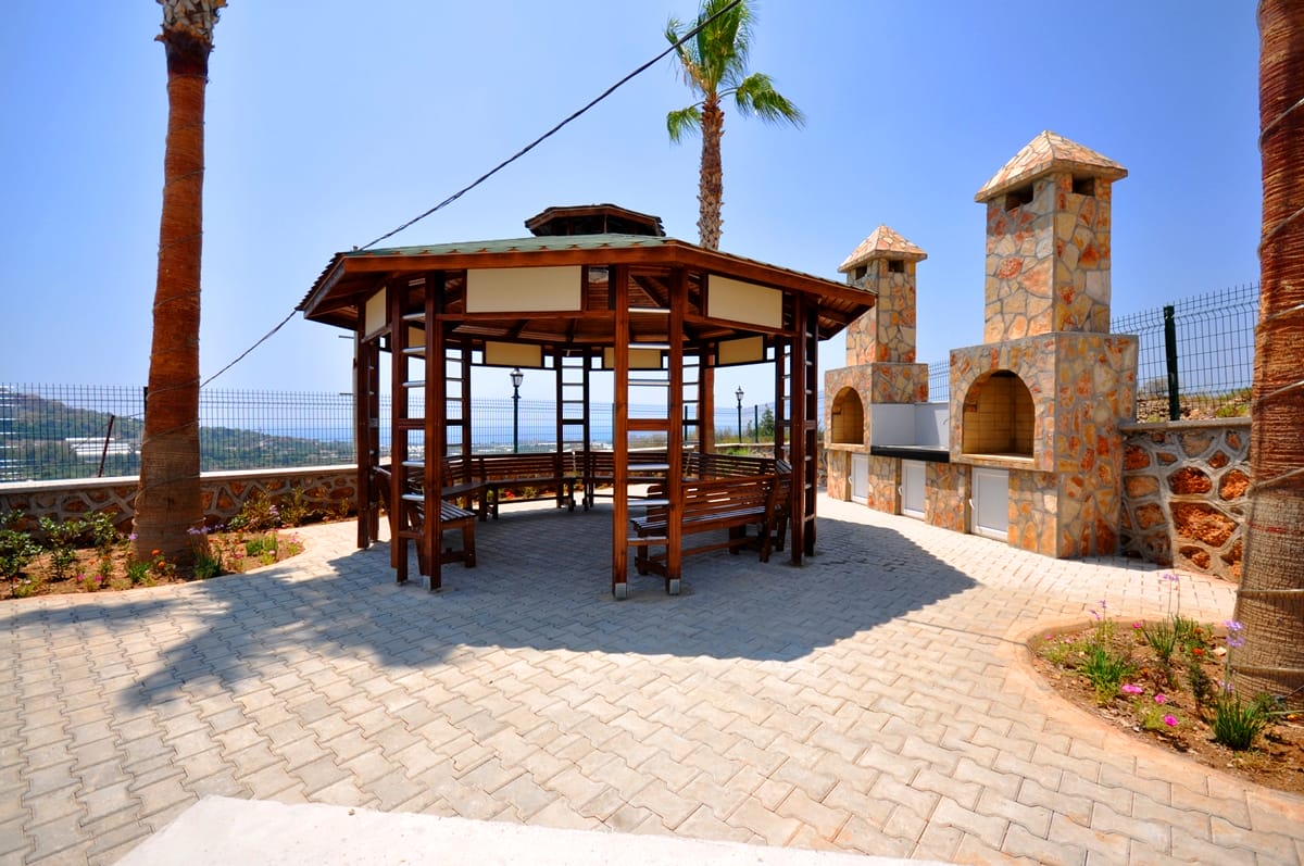 Wooden gazebo with stone barbecue ovens and palms on the grounds of a villa complex in Turkey