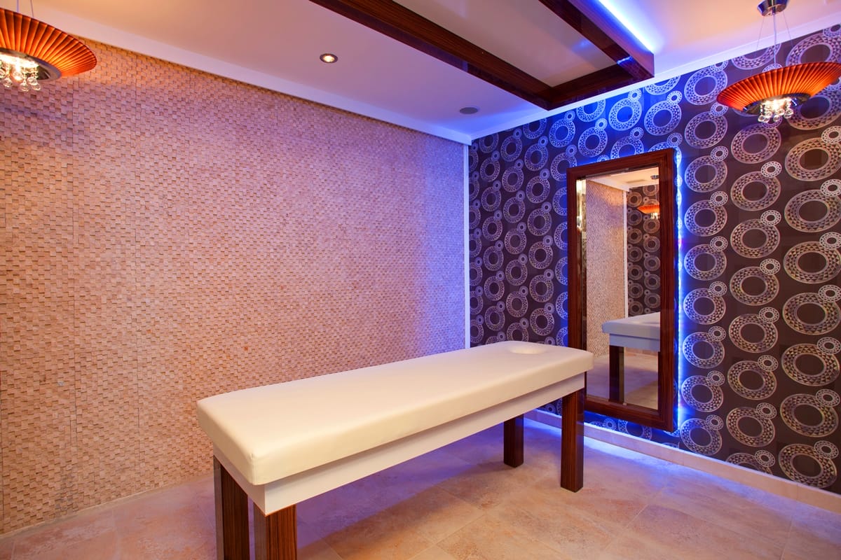 Spa area with a massage table, beige mosaic walls and blue and orange LED lighting