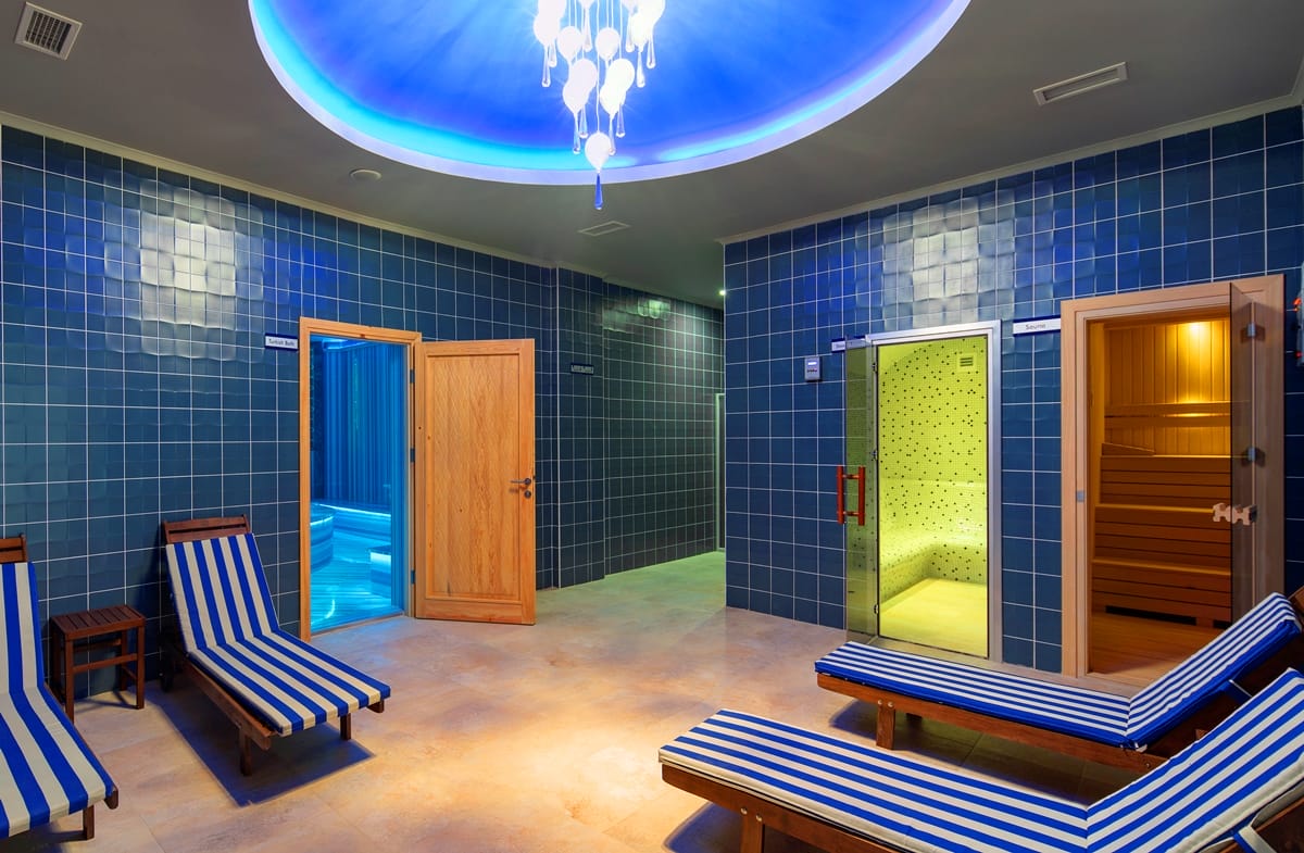 Blue-walled spa area with striped loungers and a green-lit glass cabin in a complex with villas in Kargicak
