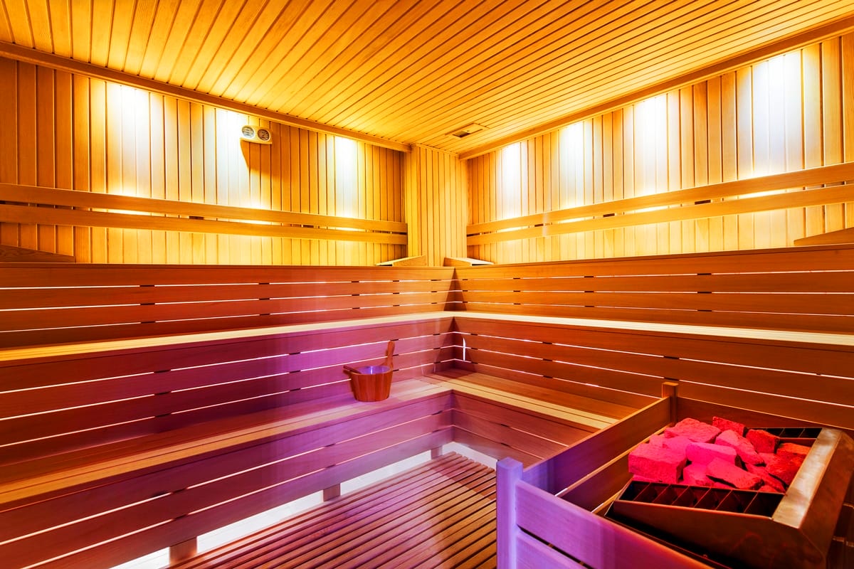 Sauna with tiered wooden benches, a stone heater and warm orange lighting in a complex with detached homes