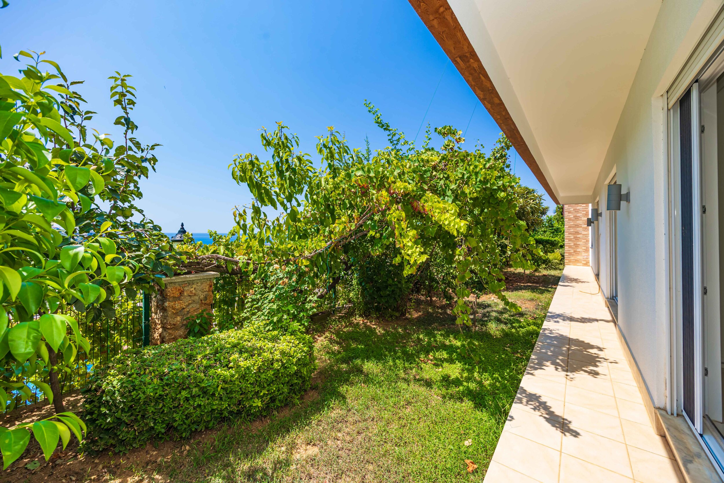 Covered walkway beside a villa and a green garden with partial sea views in Turkey for sale