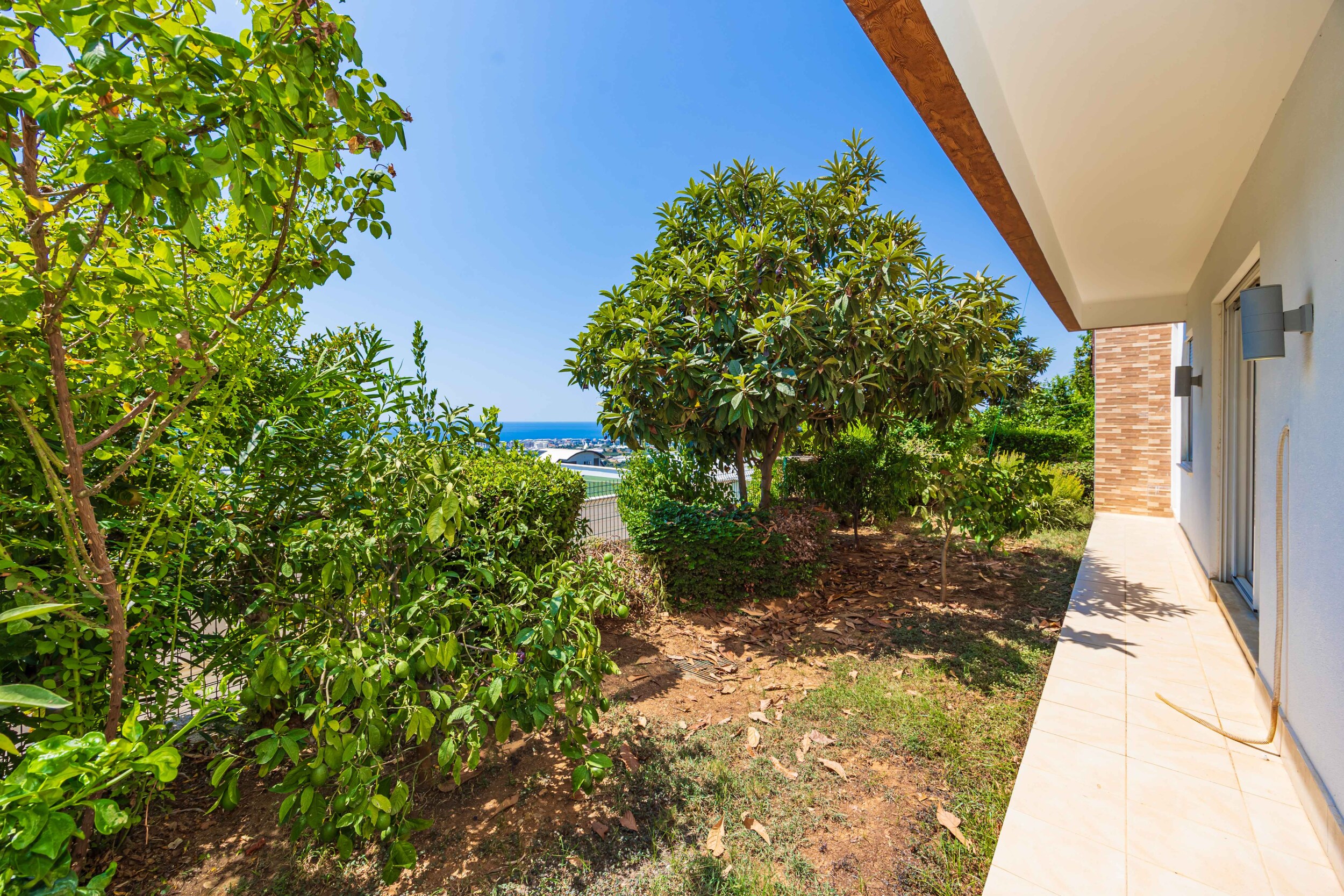 Tiled path beside a house and a dense garden with partial sea views in Turkey