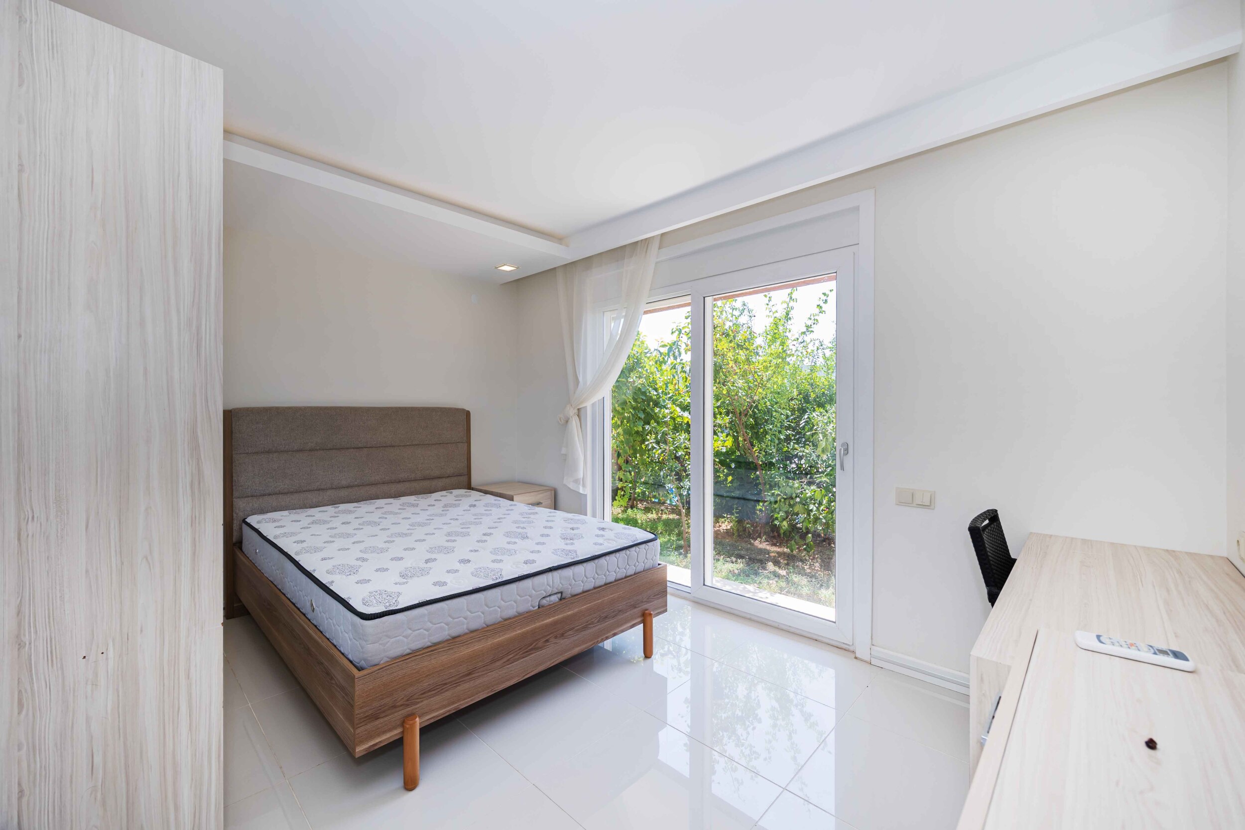 Bedroom with a double bed, desk and panoramic glass door inside the house