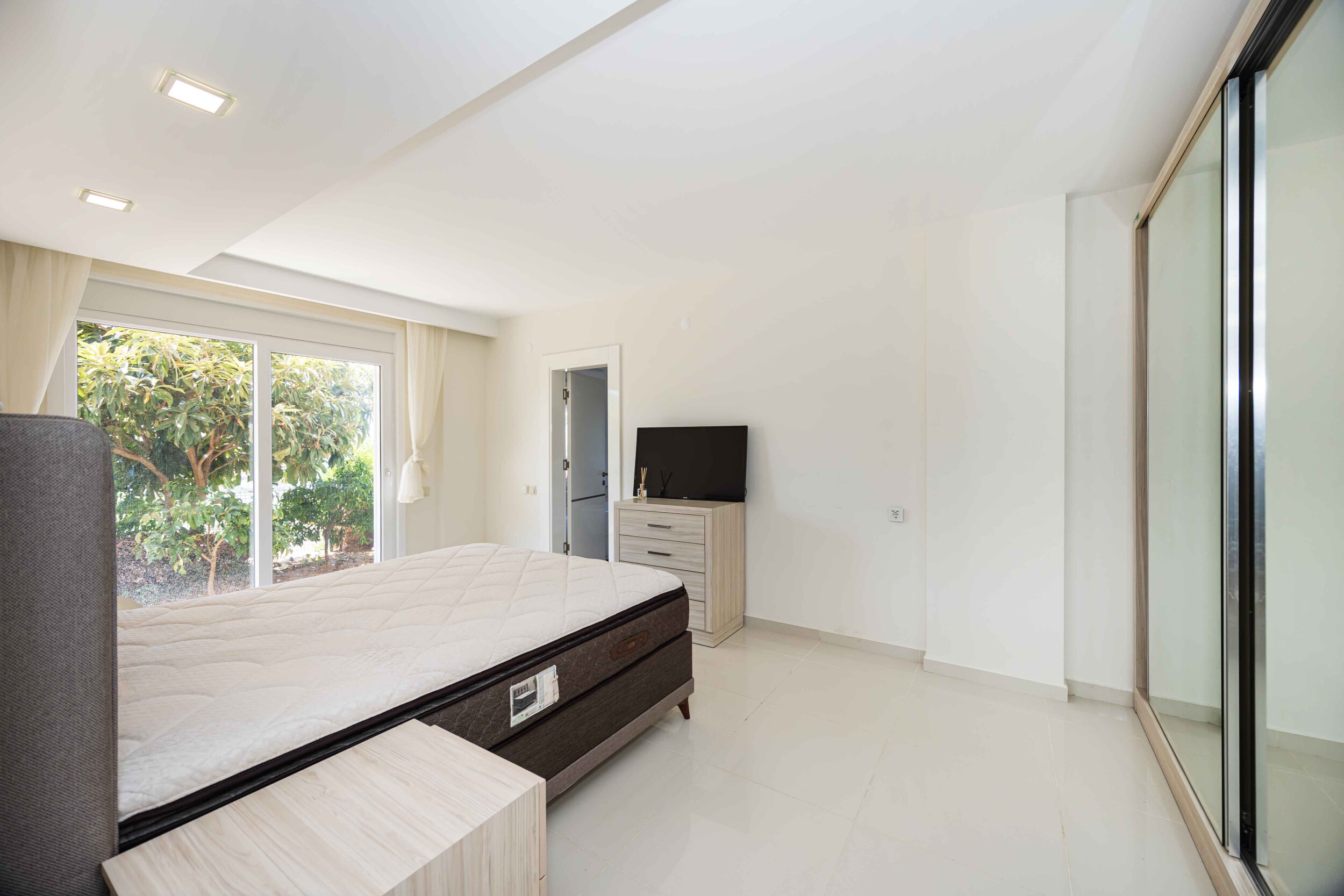 Bedroom with a double bed, mirrored wardrobe and panoramic garden window in a villa