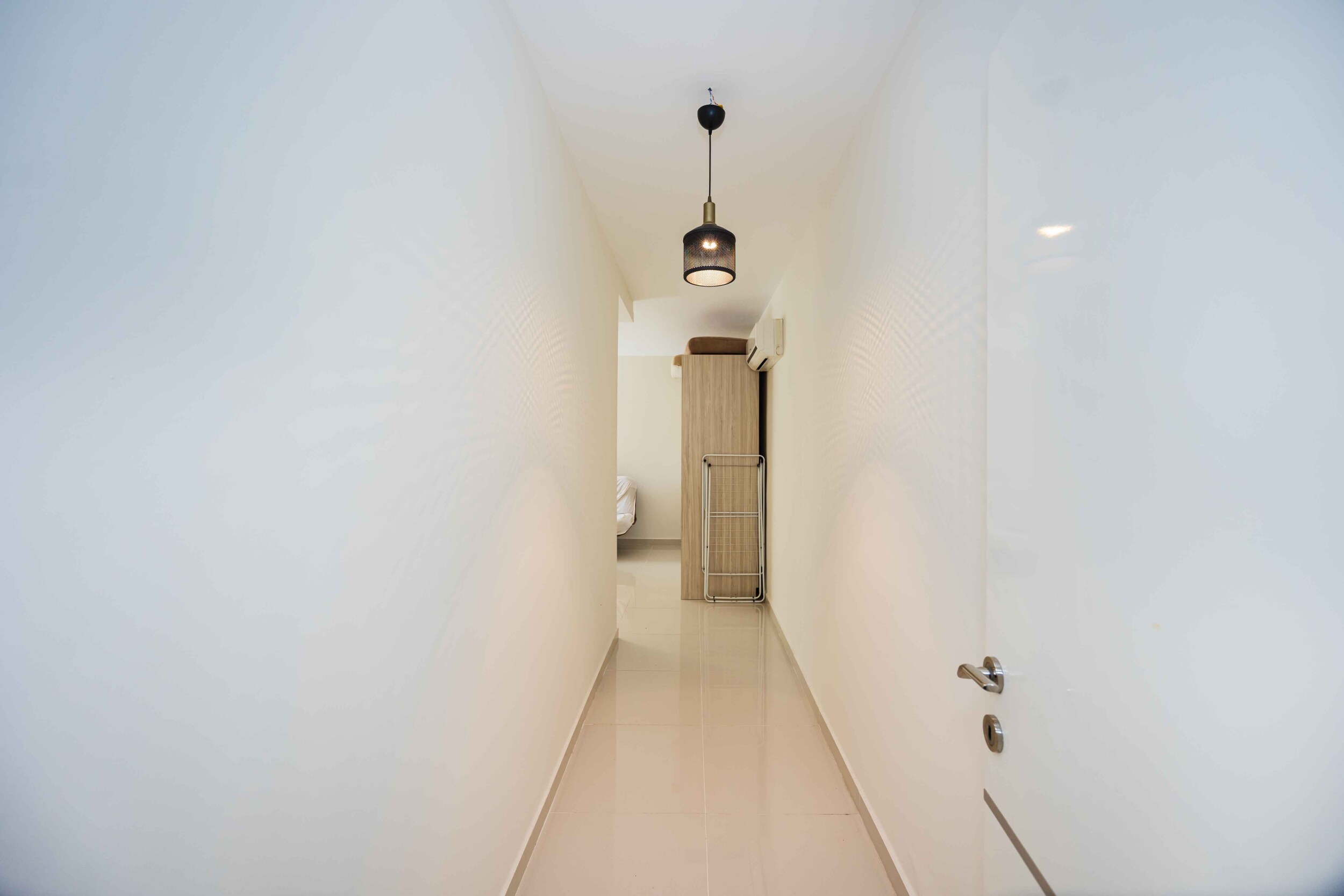 Narrow hallway with glossy flooring, white walls and a wooden door inside the house