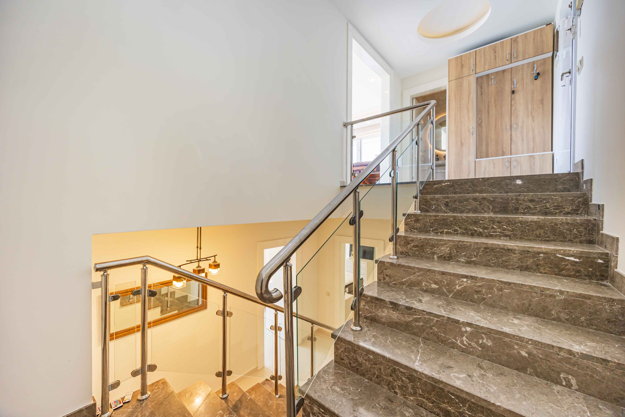 Staircase with marble steps, glass railing and built-in wardrobe in a house in Kargicak