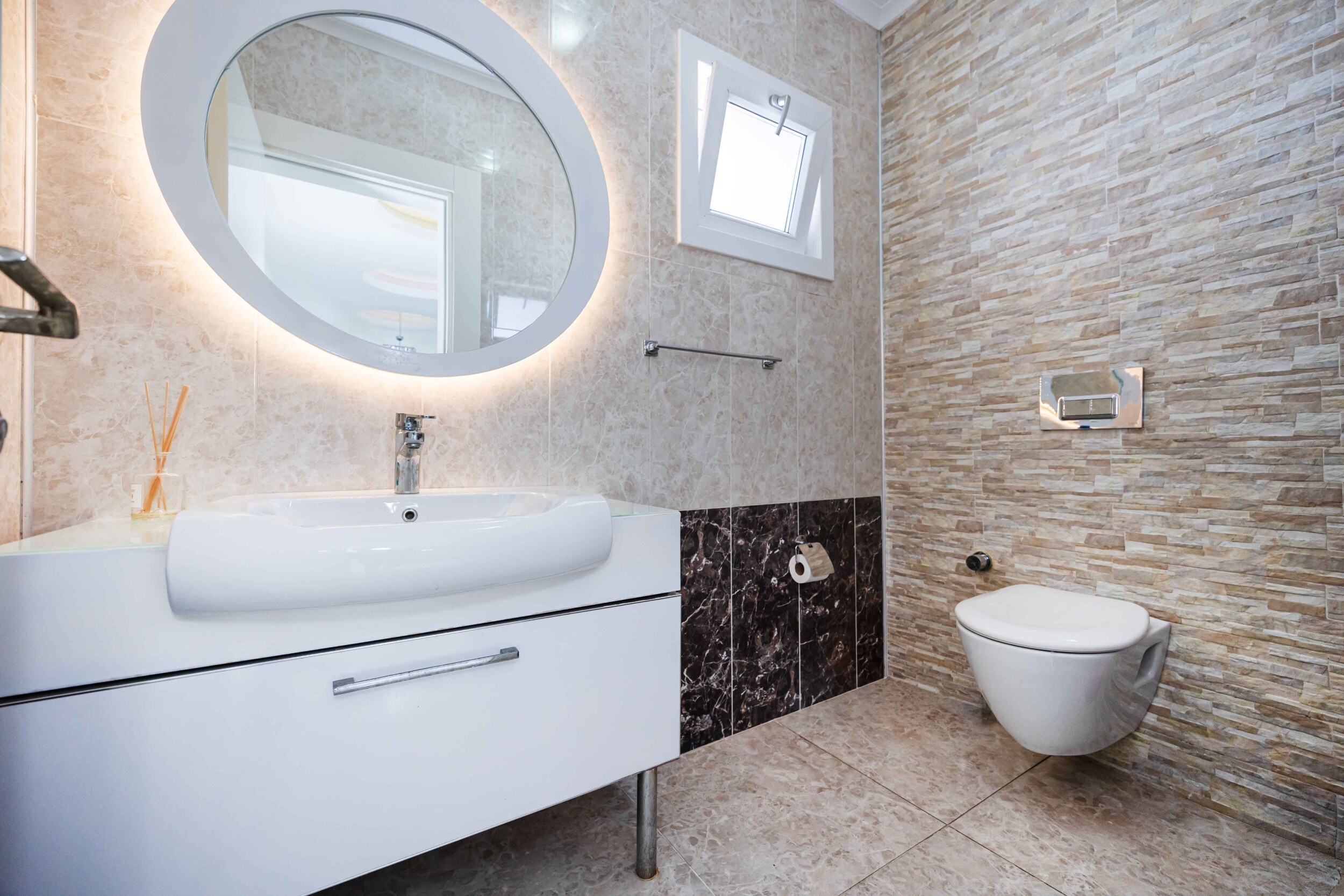 White vanity with round mirror and stone-effect tiles in the bathroom