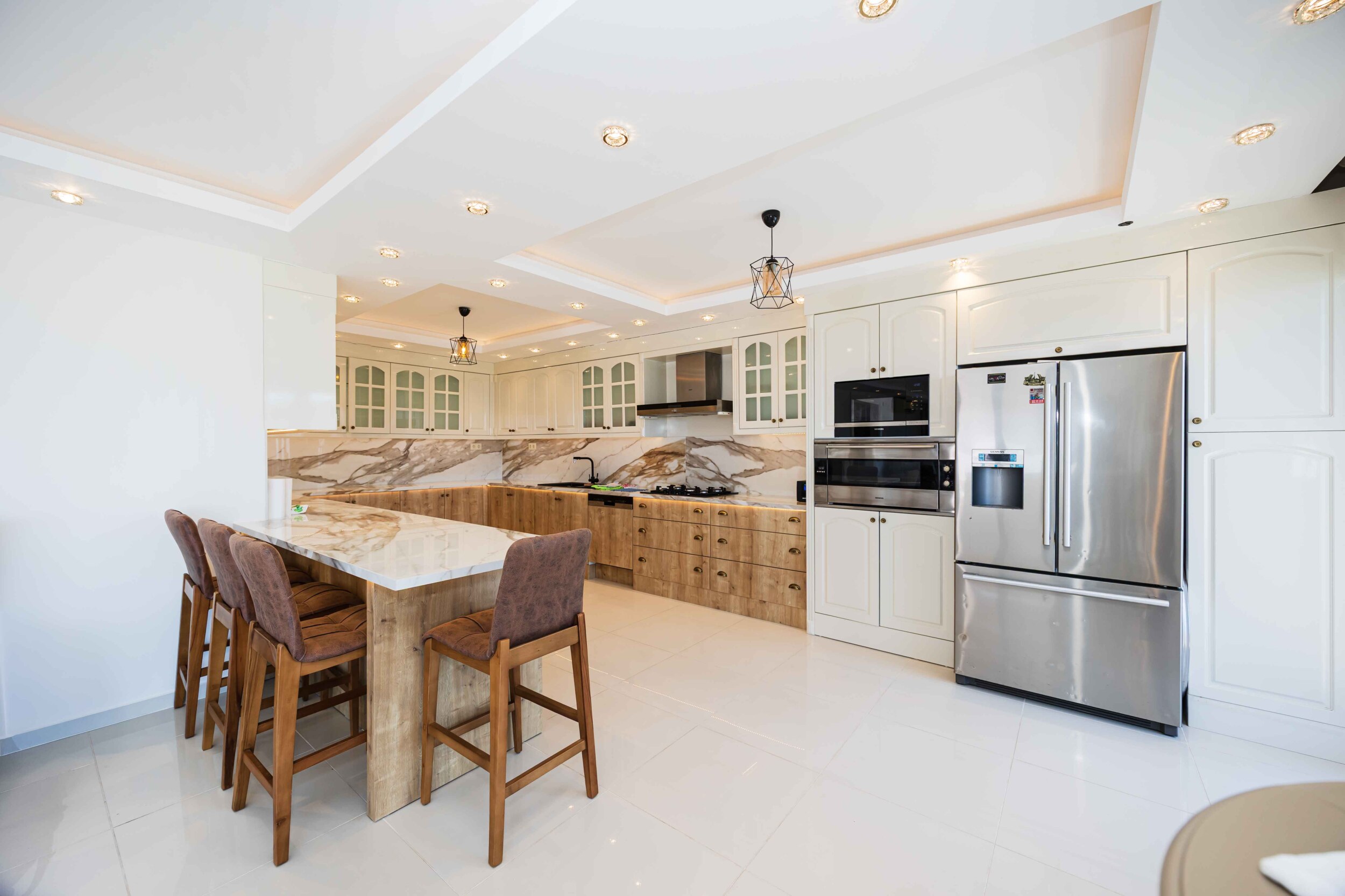 White kitchen with wooden cabinets, island and marble worktop in a house in Kargicak
