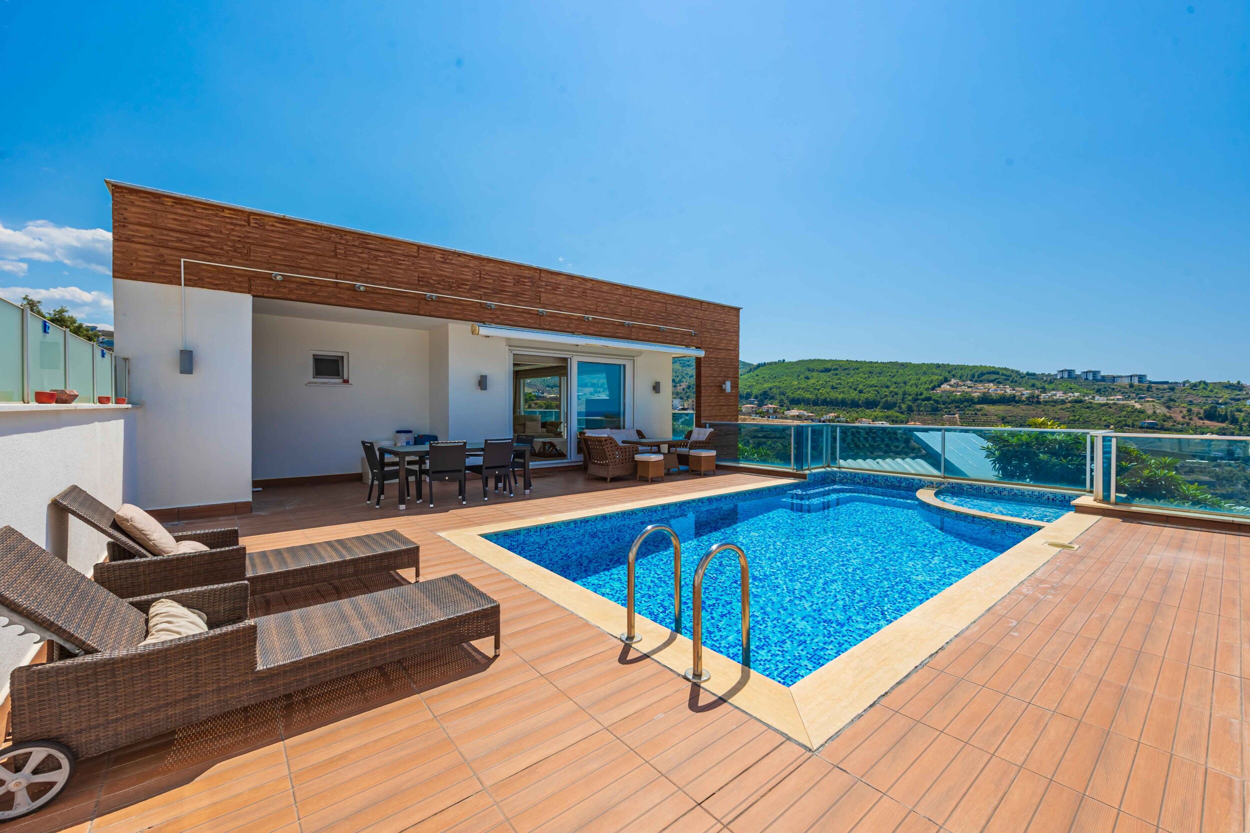 Rectangular pool with wooden terrace and dining area beside a villa for sale
