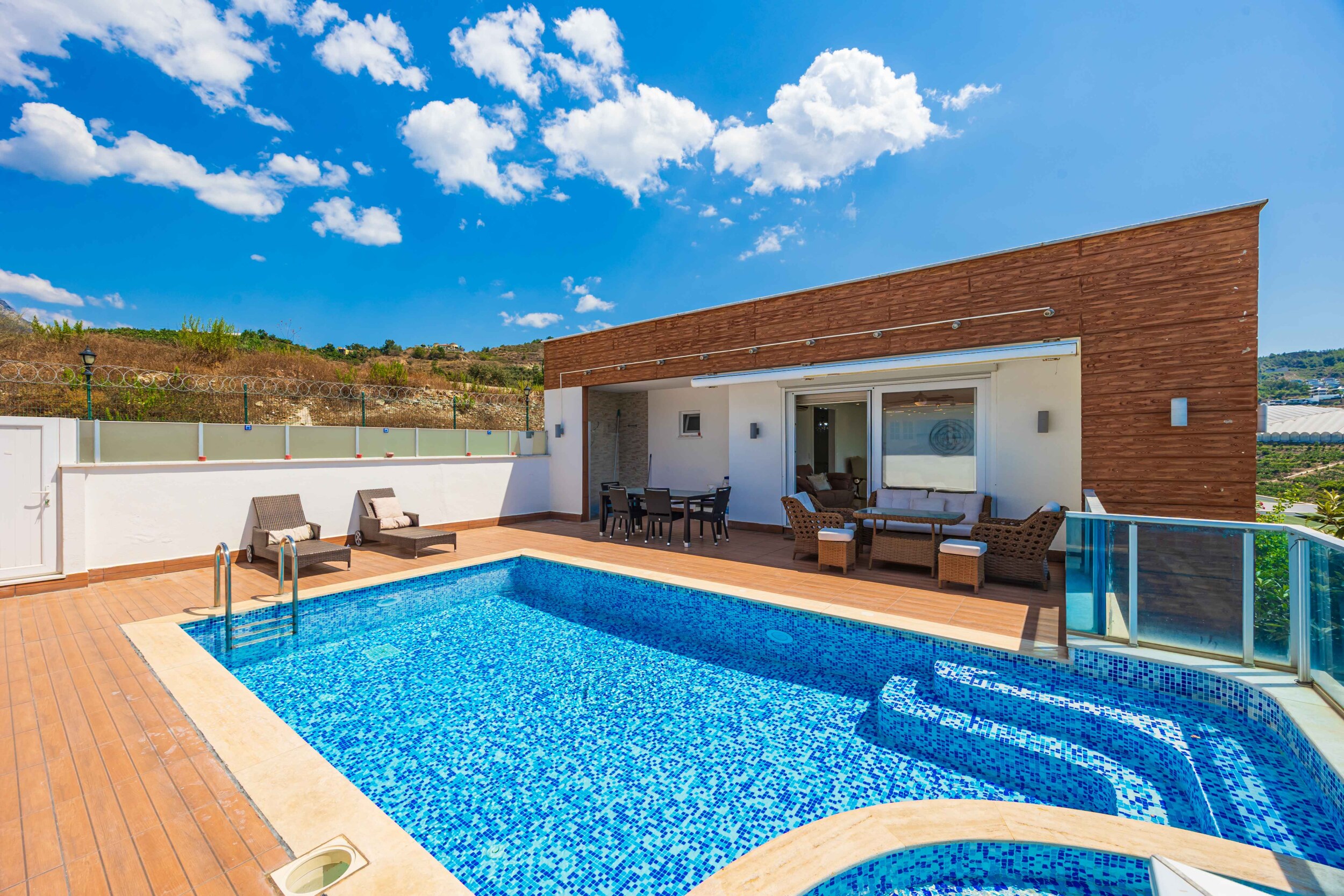 Pool with whirlpool area, wooden terrace and covered seating beside the house