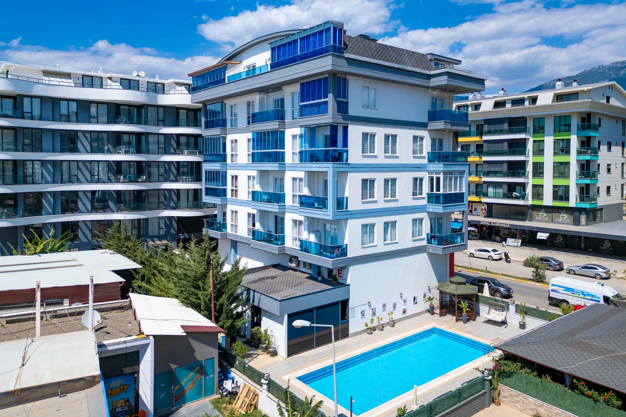 White facade with blue balconies and a pool beside a top-floor apartment in Turkey
