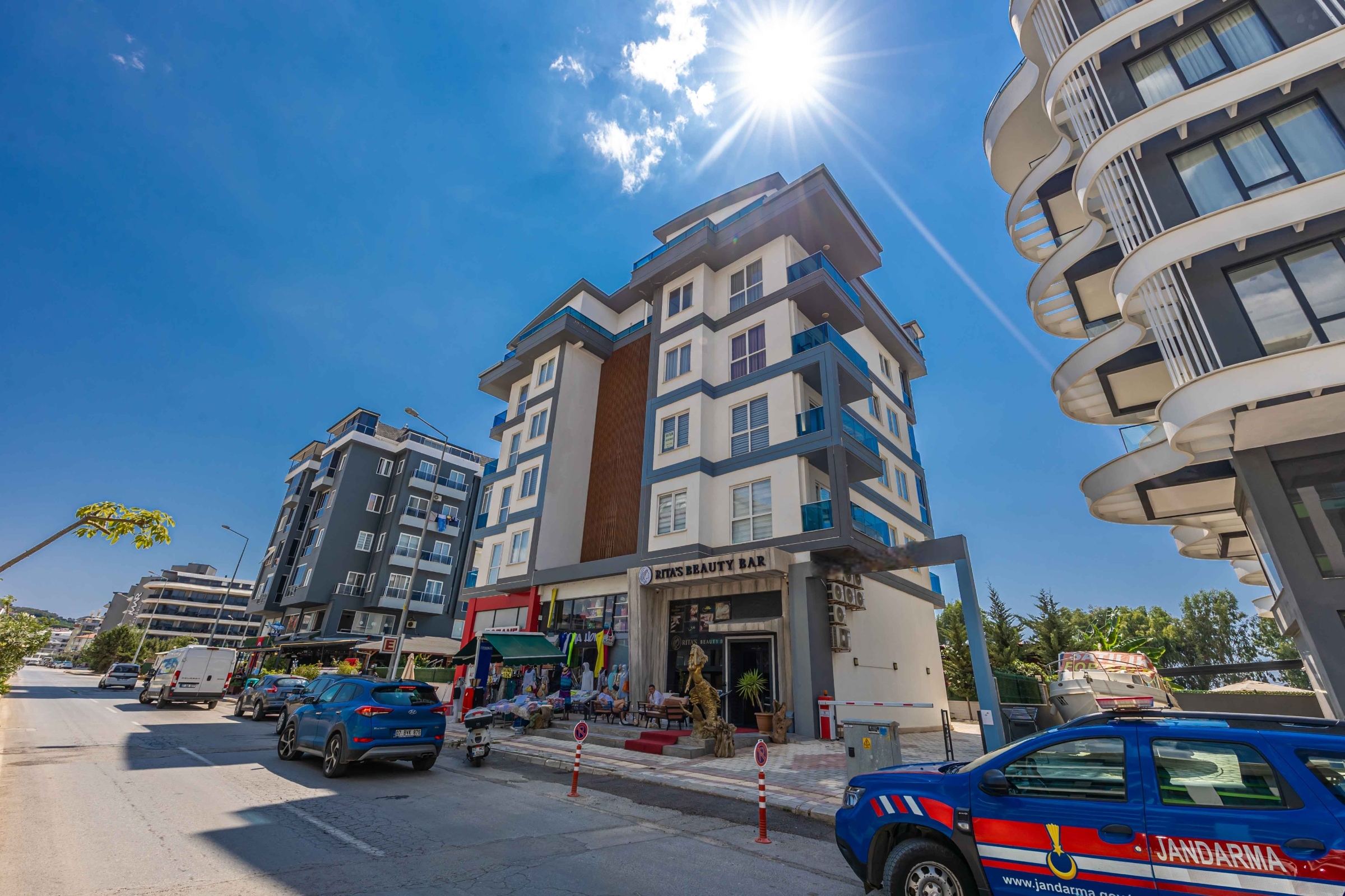 White residential building with shops and blue balconies in Kargicak against a mountain slope