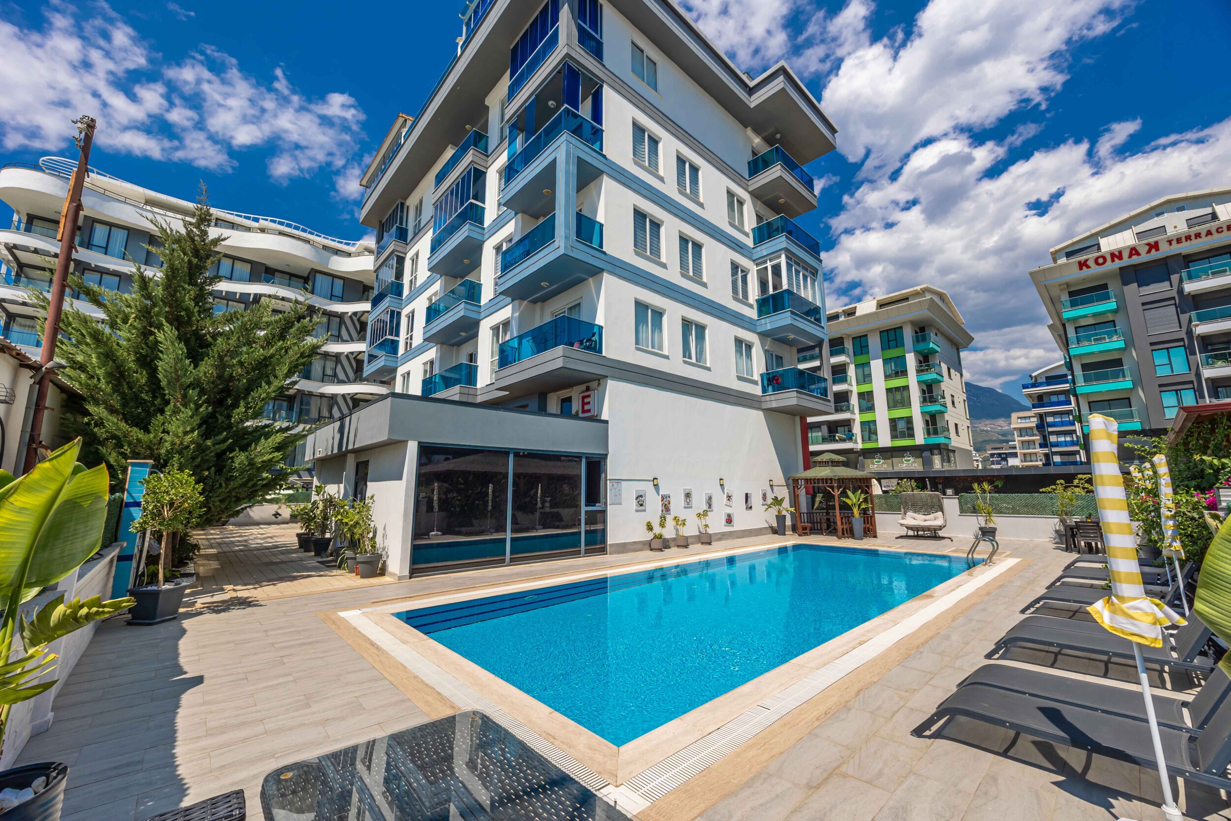 Open pool with loungers and a white facade at a complex with apartments in Kargicak, Turkey
