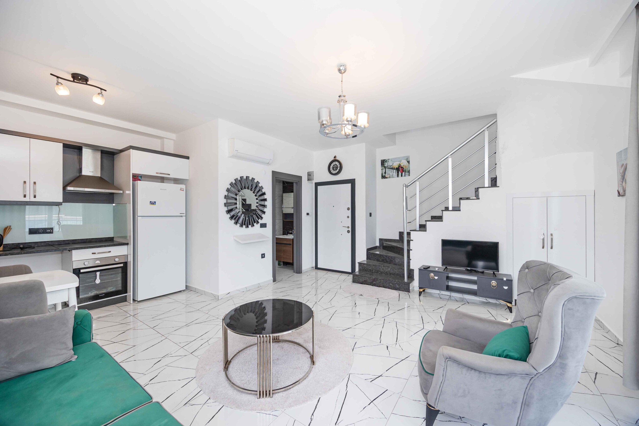 Living room with a green corner sofa, white kitchen and stairs in a duplex for sale