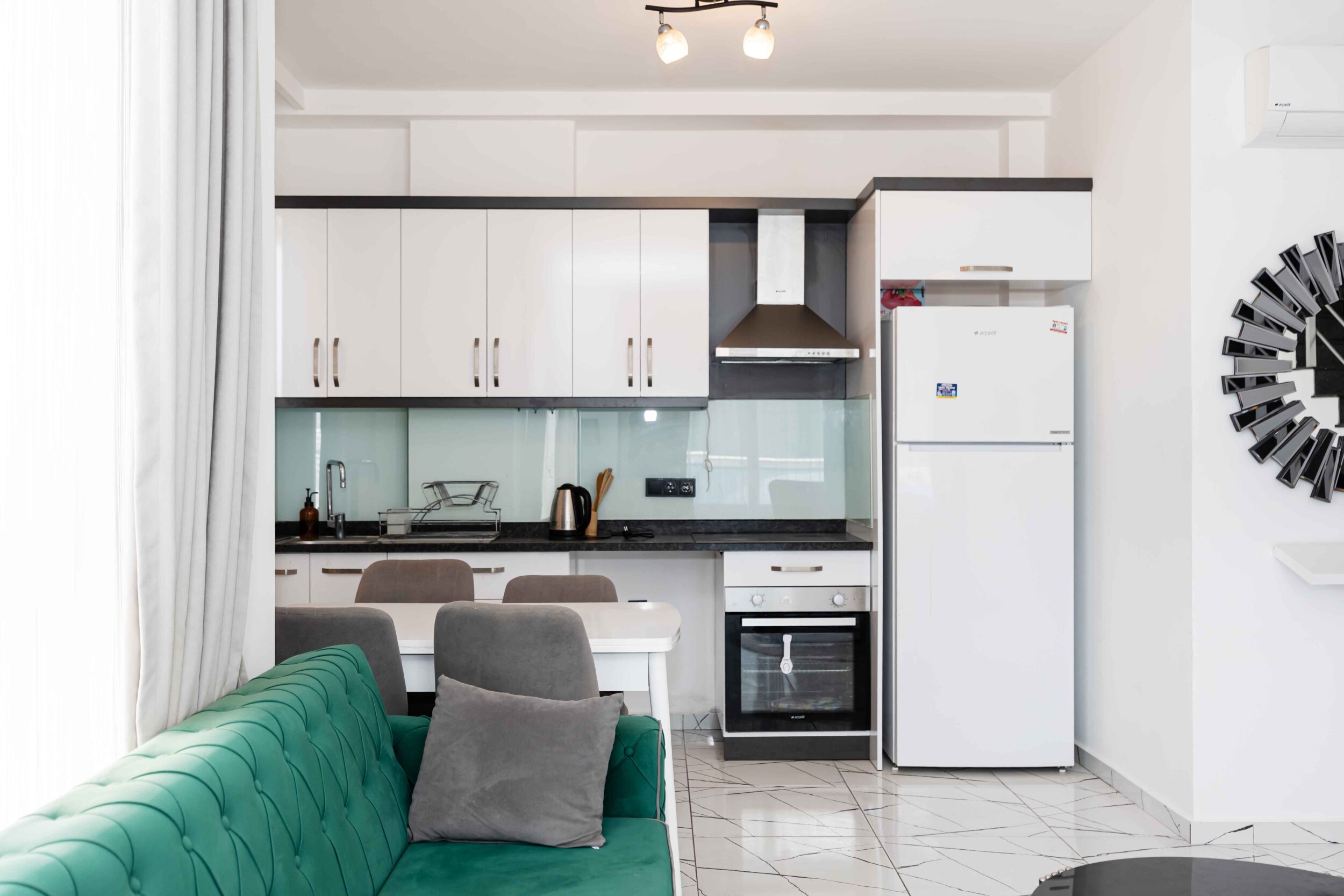 Linear white kitchen with black worktop and green sofa in a residential interior