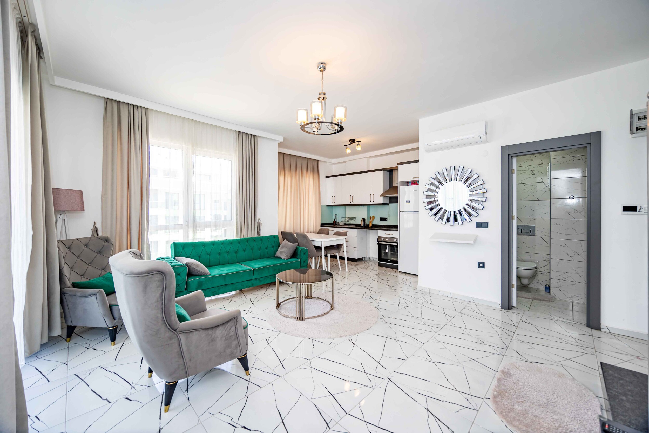 Green sofa, gray armchairs and white kitchen zone in a residence in Kargicak