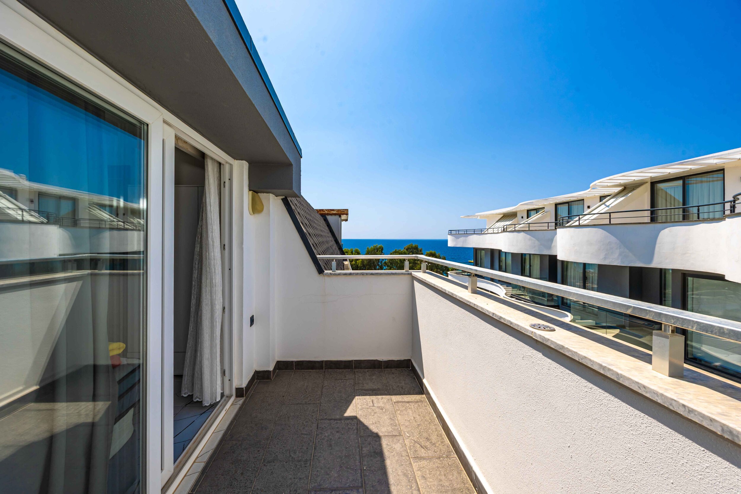 Open terrace with glass railing and a strip of sea beside a penthouse