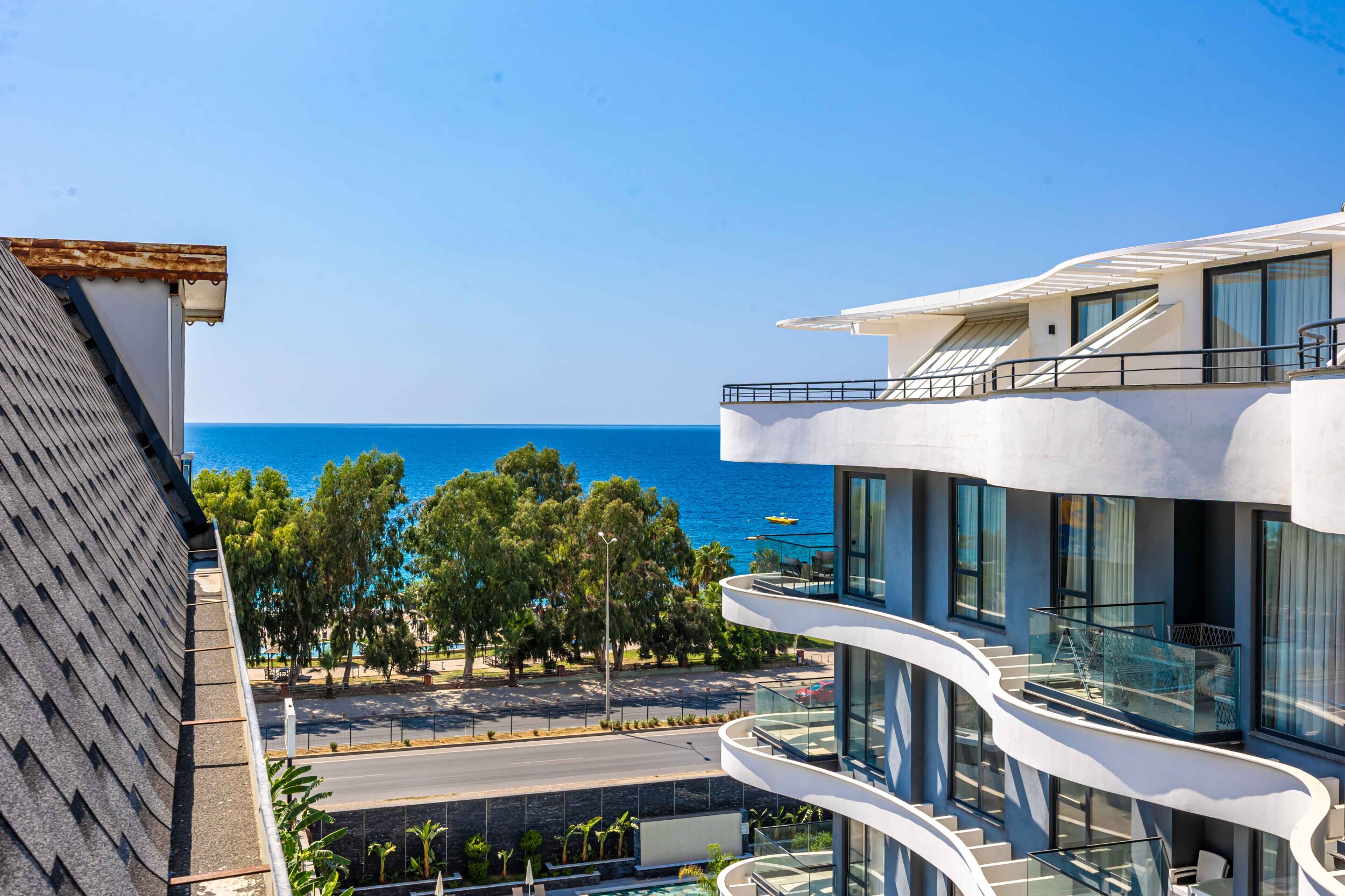 Sea behind trees and a white building with curved balconies beside apartments for sale in Turkey