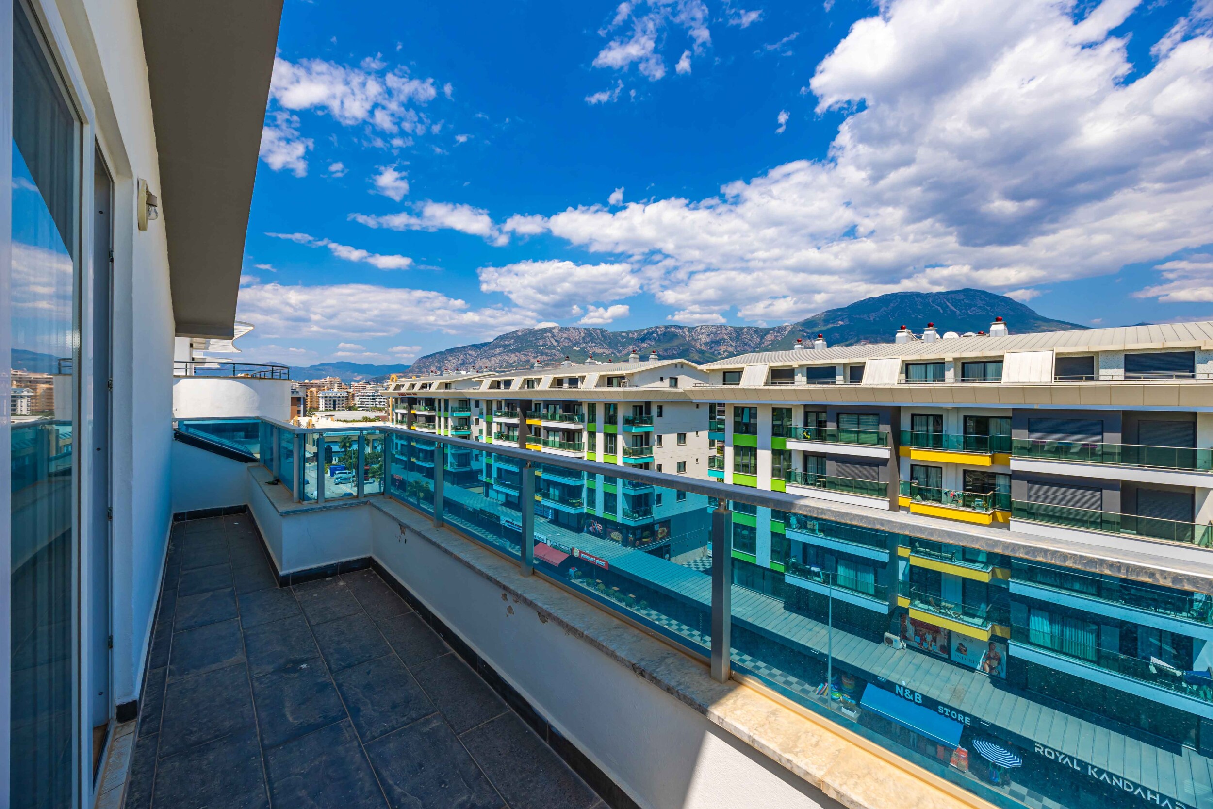 Long balcony with glass railing and mountain views beside a penthouse for sale