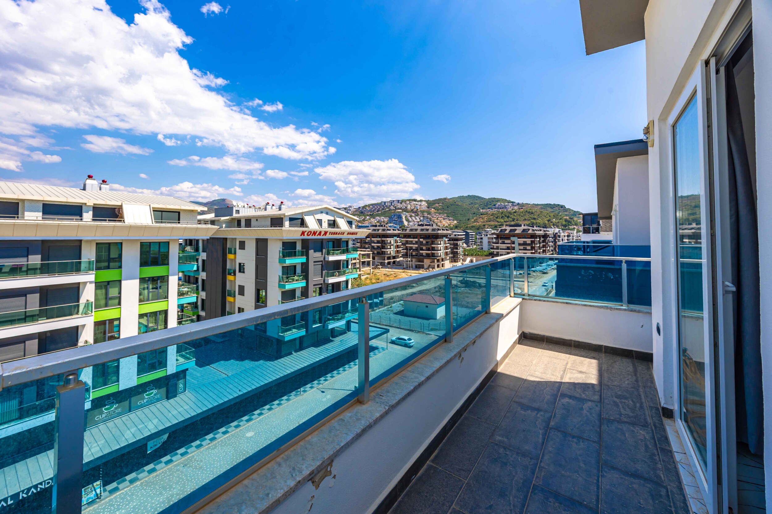 Narrow balcony with glass railing and mountain landscape beside apartments in Kargicak, Turkey