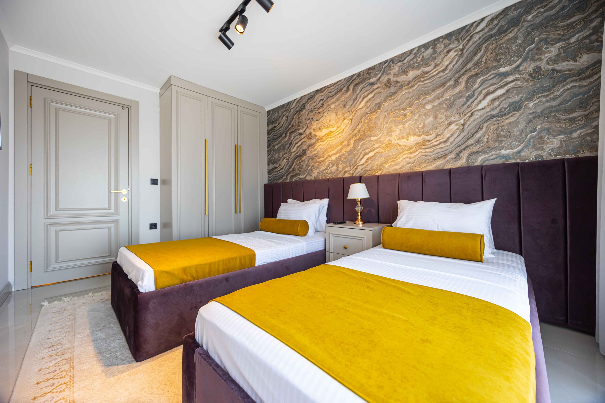 Спальня с двумя кроватями, горчичными покрывалами и мраморной стеной в вилле в Оба