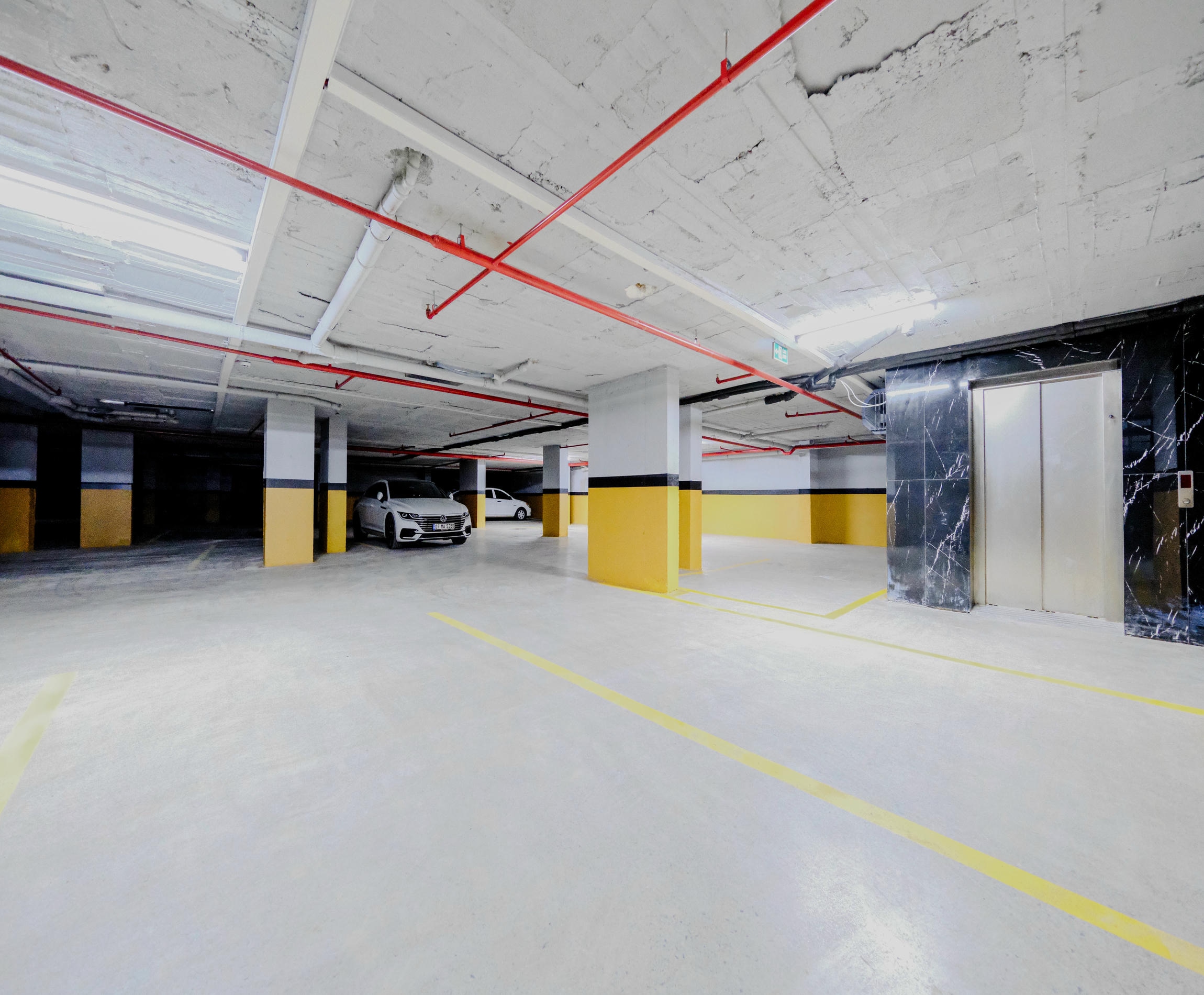 Underground parking with yellow bay markings and a marble-clad lift near a top-floor apartment by the sea