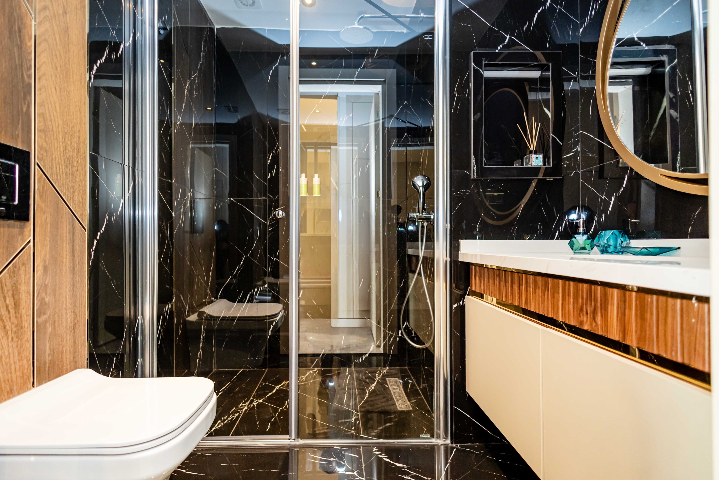 Bathroom with black marble, glass shower enclosure and round mirror in an apartment by the sea