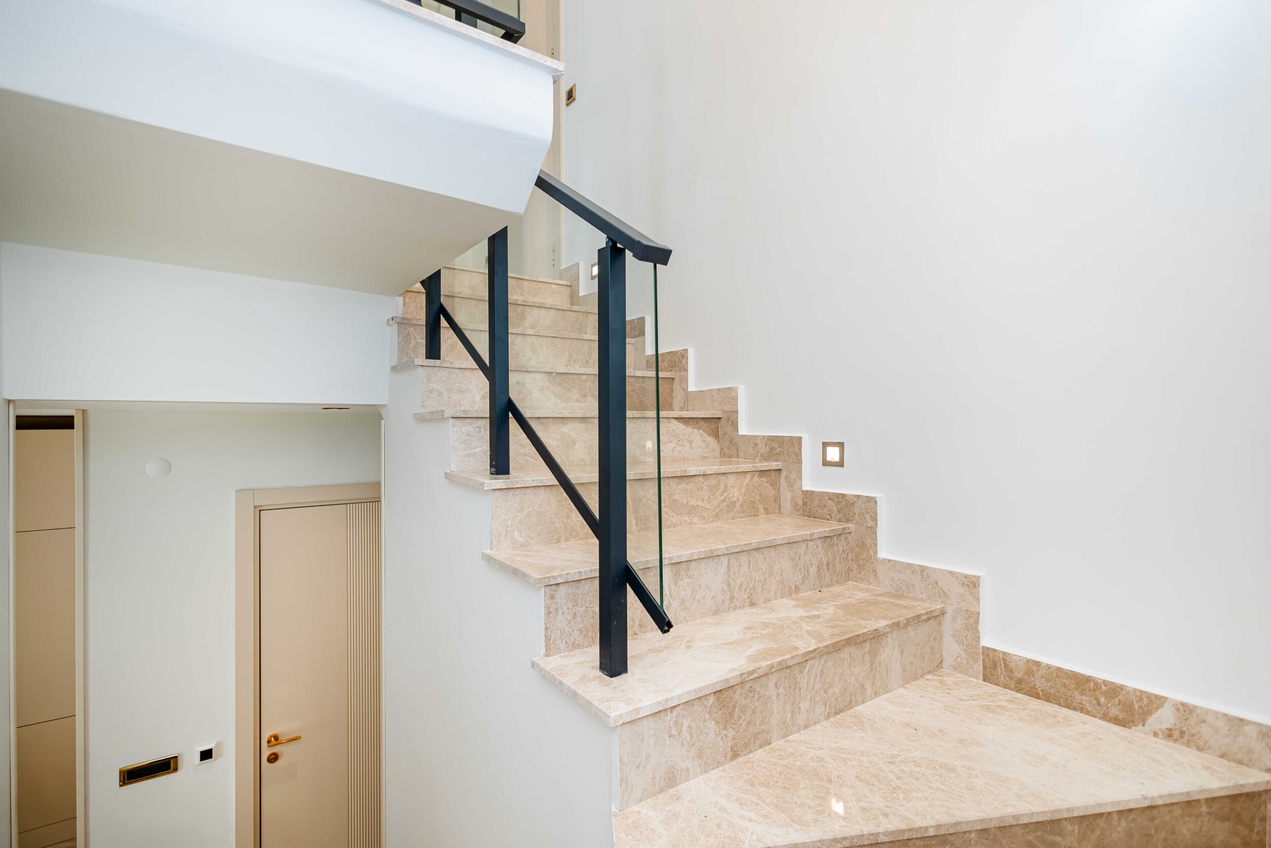 Interior staircase with marble steps, glass railing and black handrail in a top-floor apartment