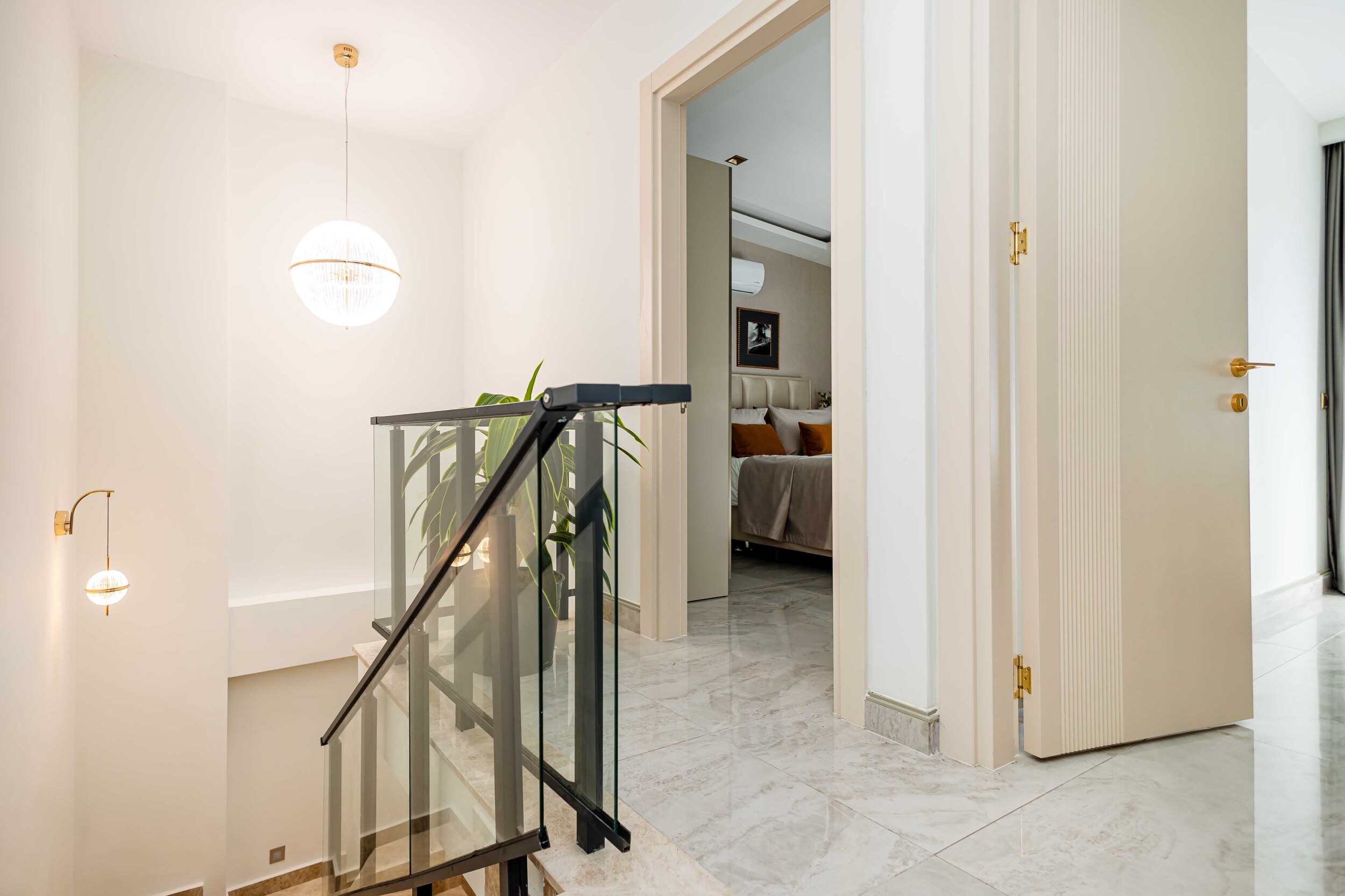 Staircase with glass railing and marble flooring leading toward a bedroom in a residence
