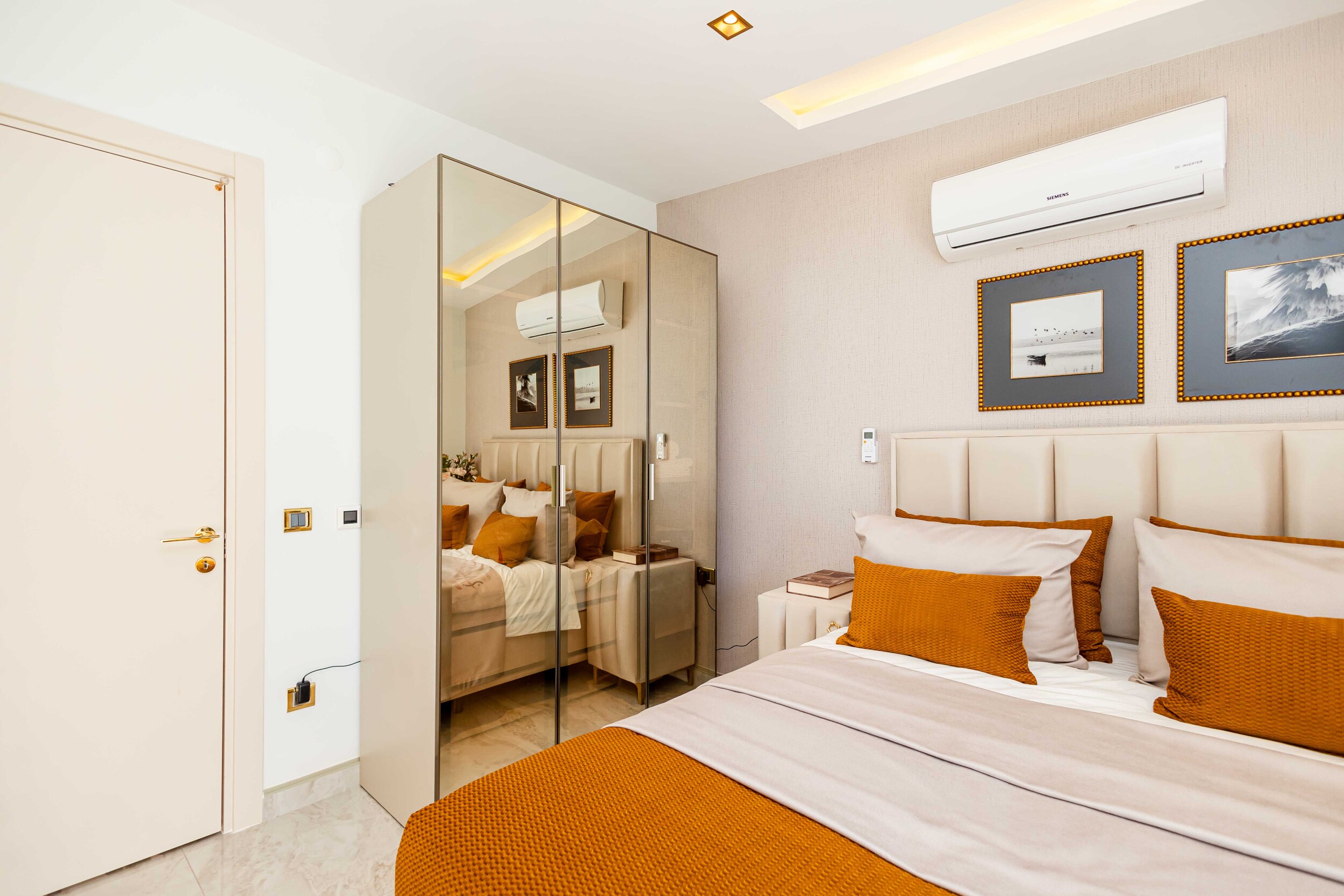 Bedroom with orange bedspread, mirrored wardrobe and framed artwork in a residence
