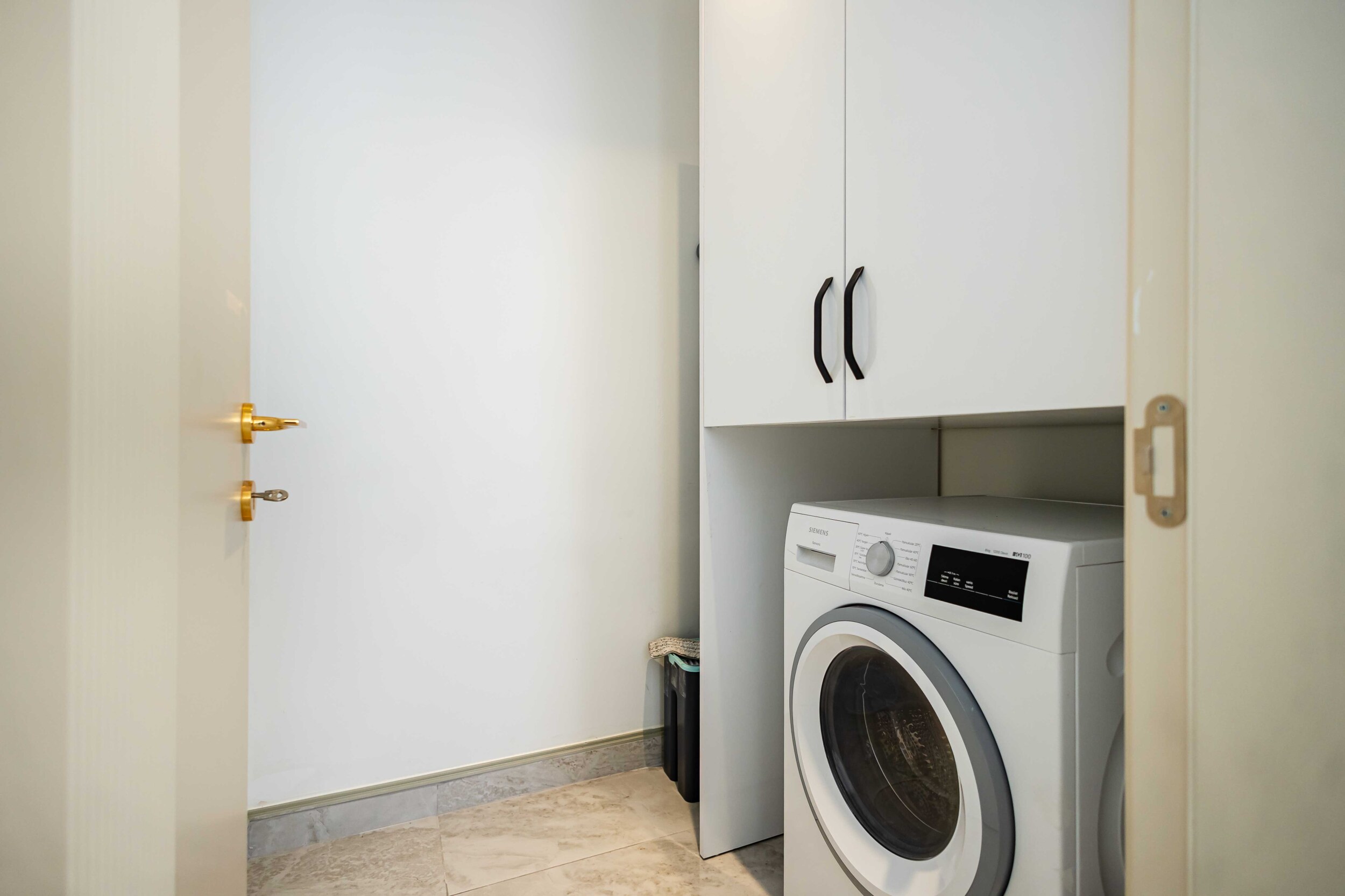 Laundry room with front-loading washing machine and tall cabinet on marble flooring
