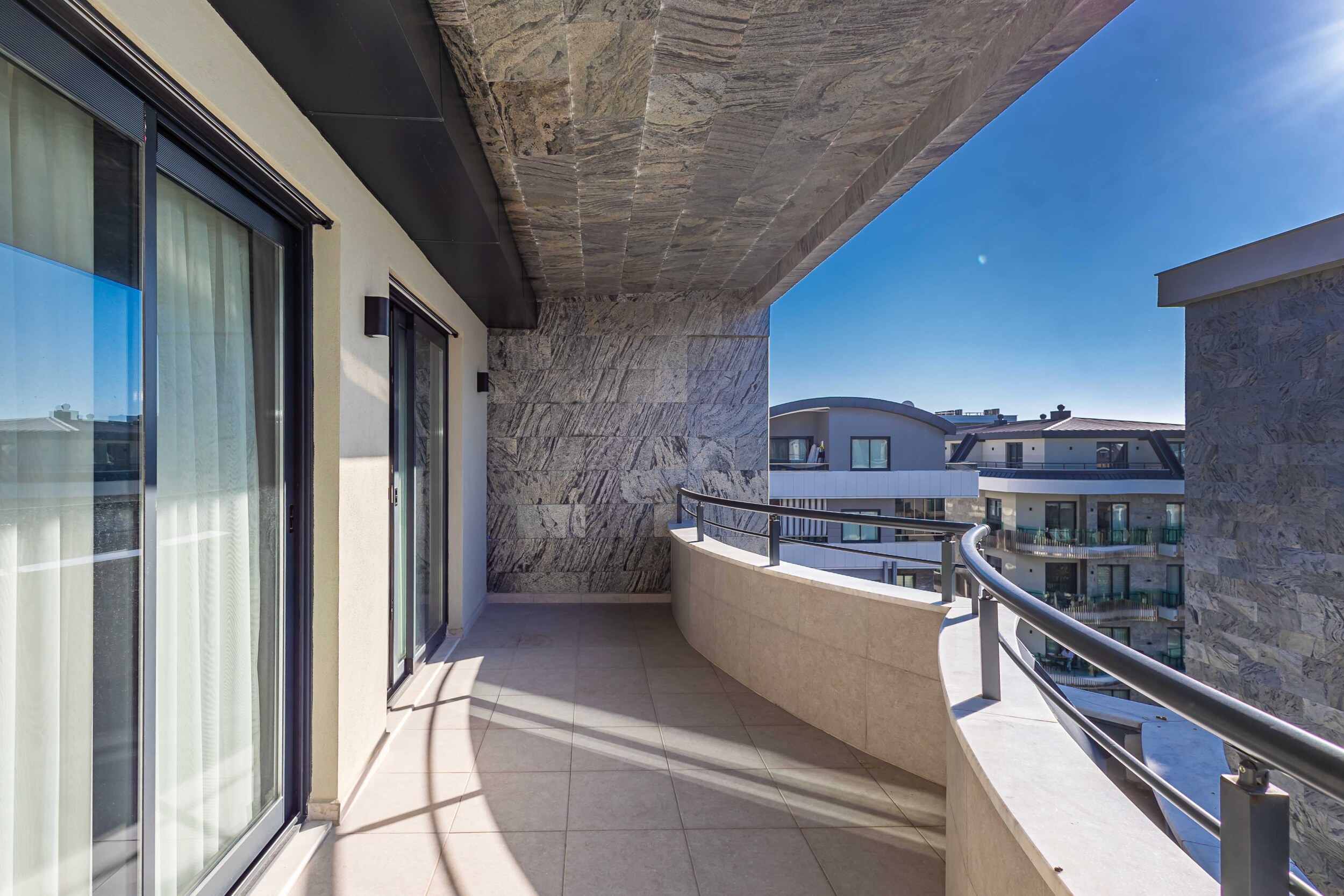Curved balcony with sliding doors and stone-look cladding at a penthouse by the sea in Turkey