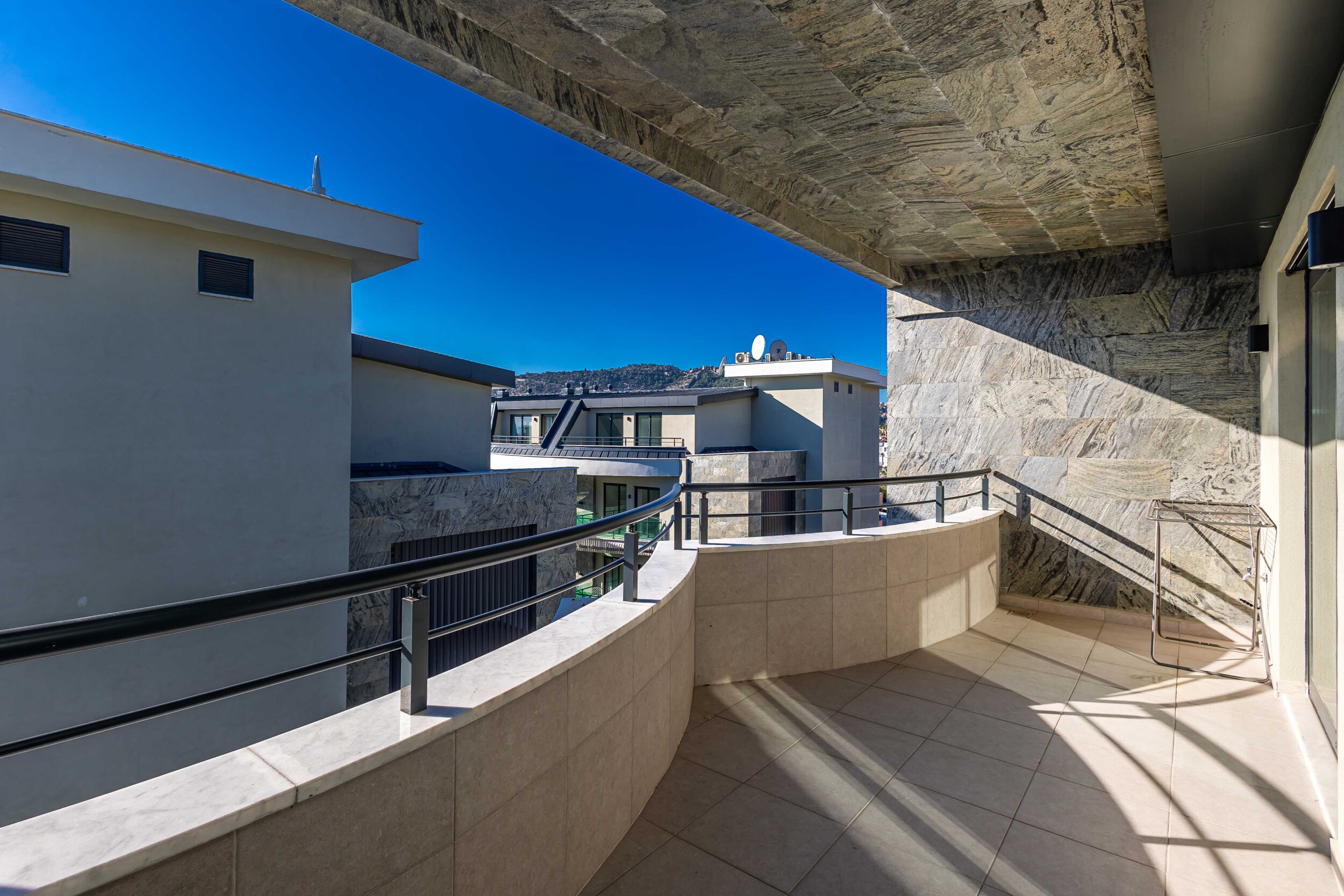 Spacious terrace with curved parapet and distant sea strip from a top-floor apartment
