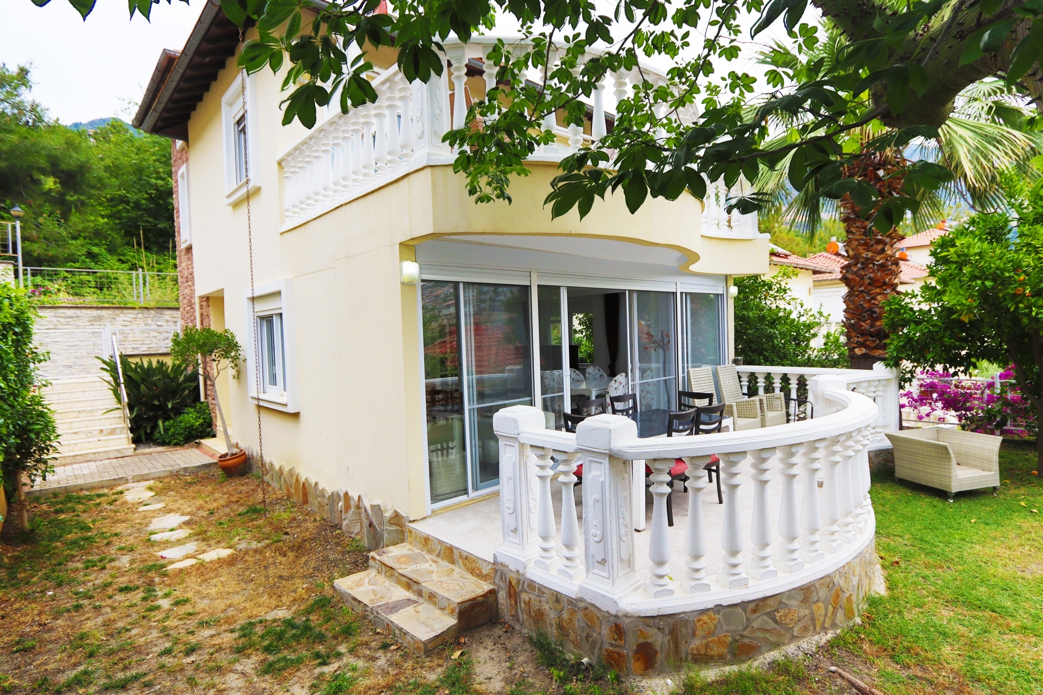 Corner villa facade with a glazed terrace, stone base and flowering shrubs in Alanya