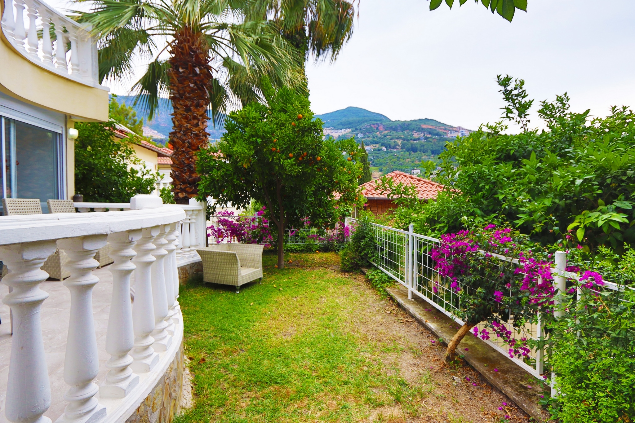 Villa garden with palms, bougainvillea and a mountain view behind the white terrace balustrade in Alanya, Turkey