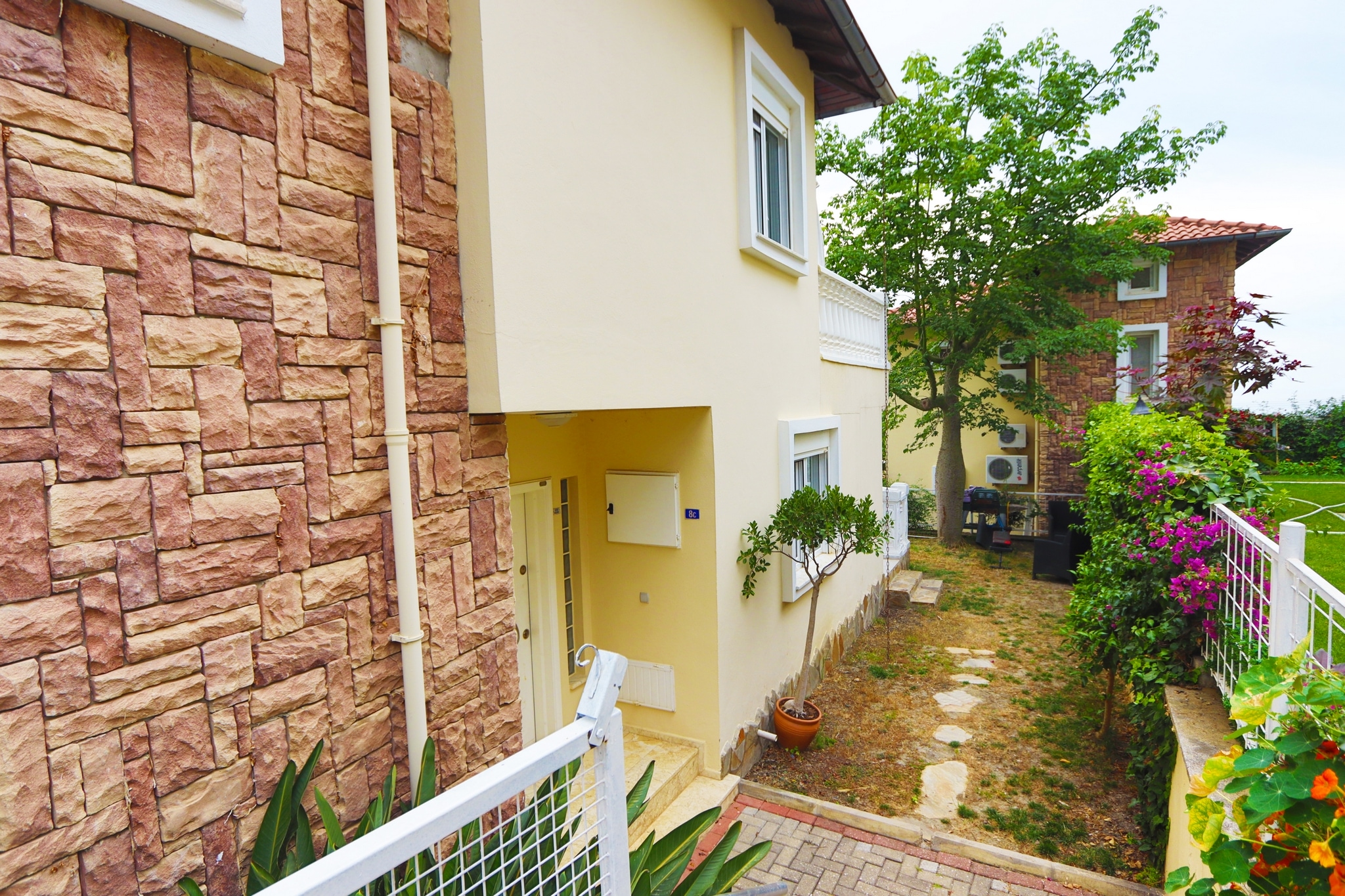Side villa facade with stone cladding, exterior stairs and a flowering garden in Alanya, Turkey