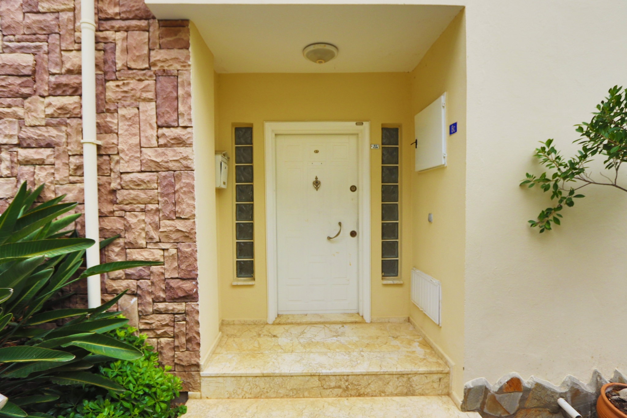 White entrance door with side glazing, marble steps and a stone-clad wall at a property for sale