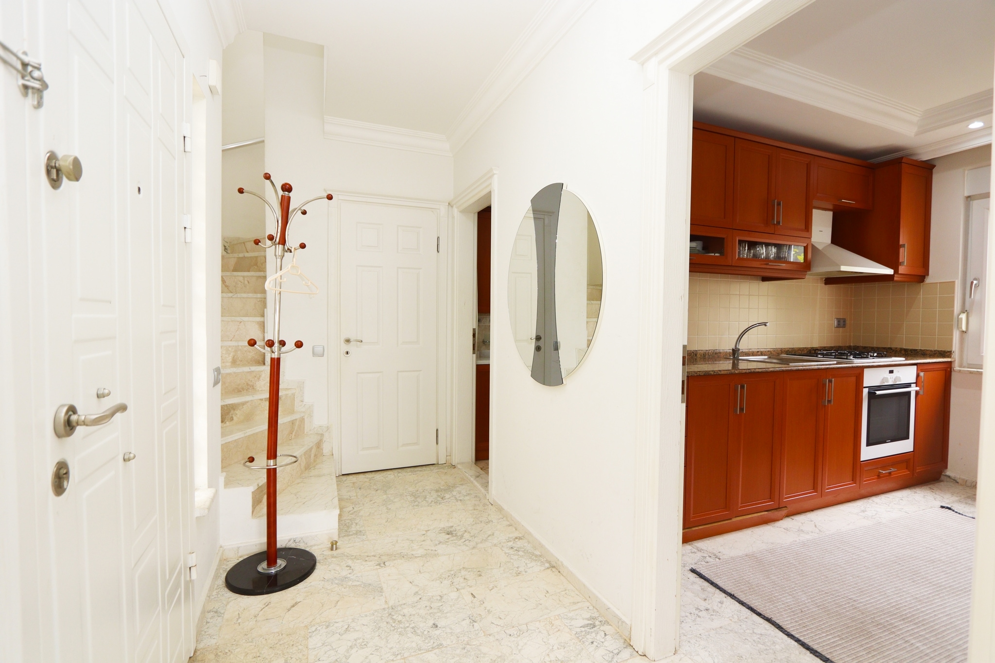 Entry hall with marble flooring, a staircase and oval wall mirror beside the white entrance door