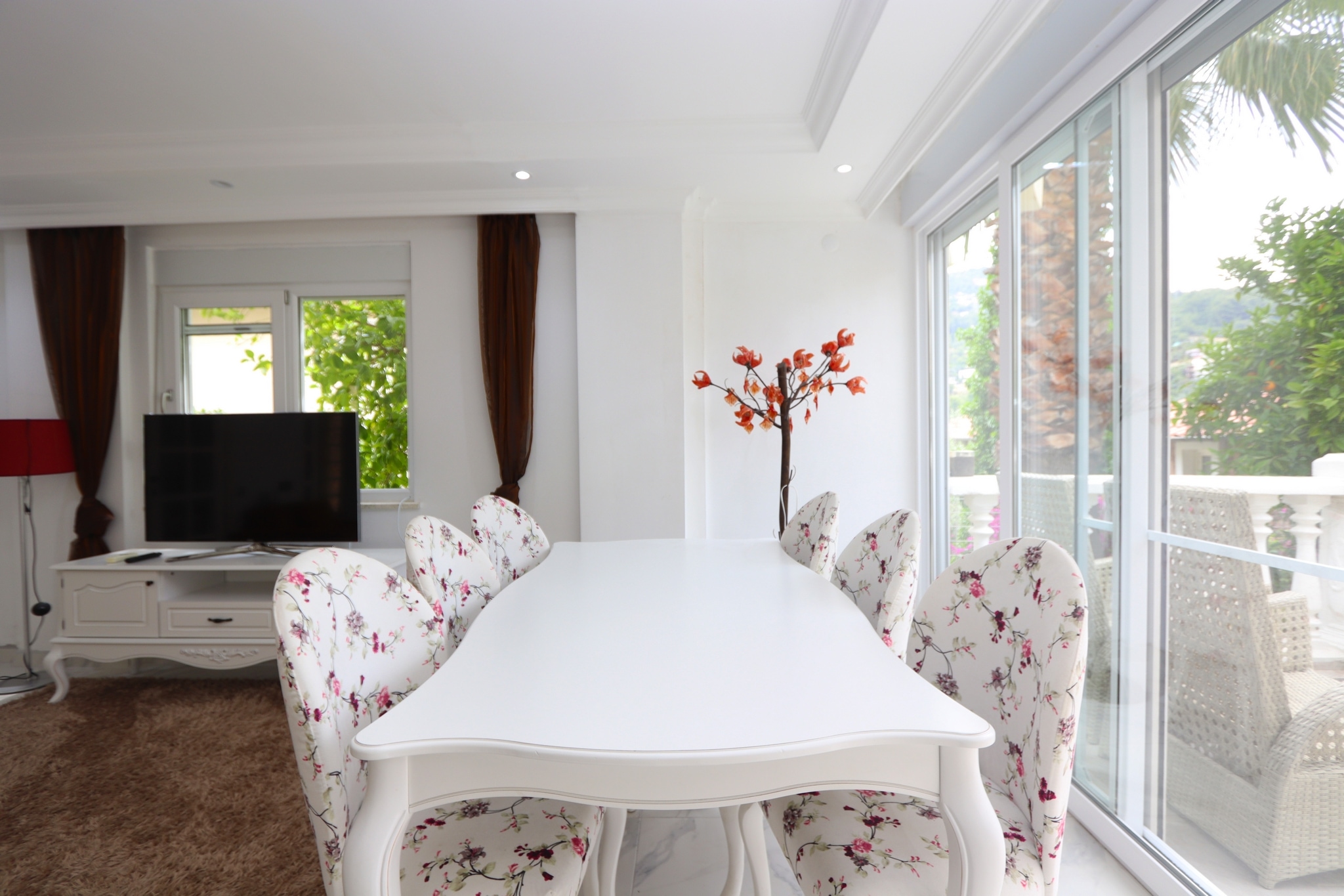 Dining room with a white table, floral chairs and panoramic windows in a villa in Alanya