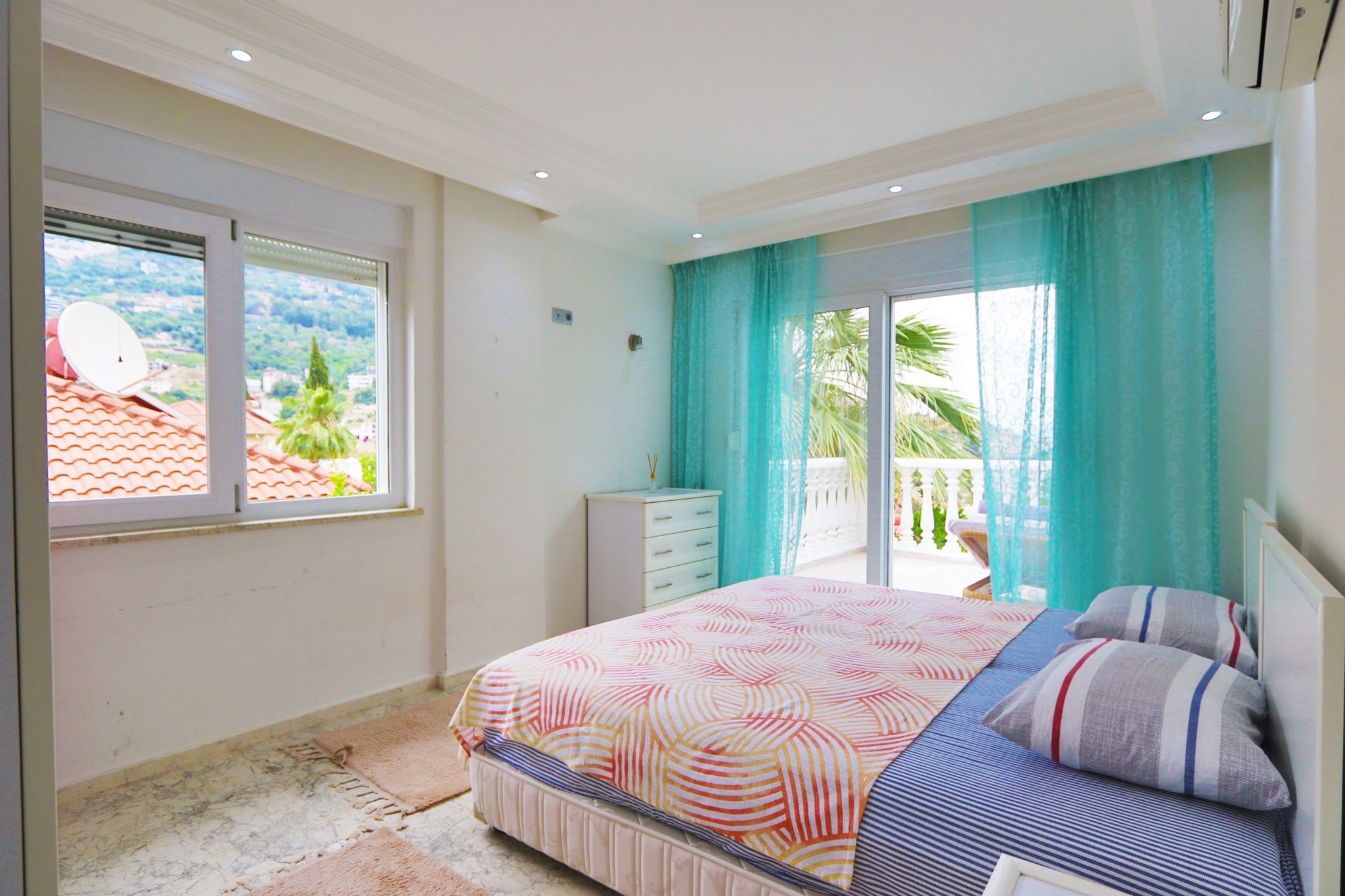 Bedroom with a double bed, chest of drawers and a view of a red-tiled roof in a villa