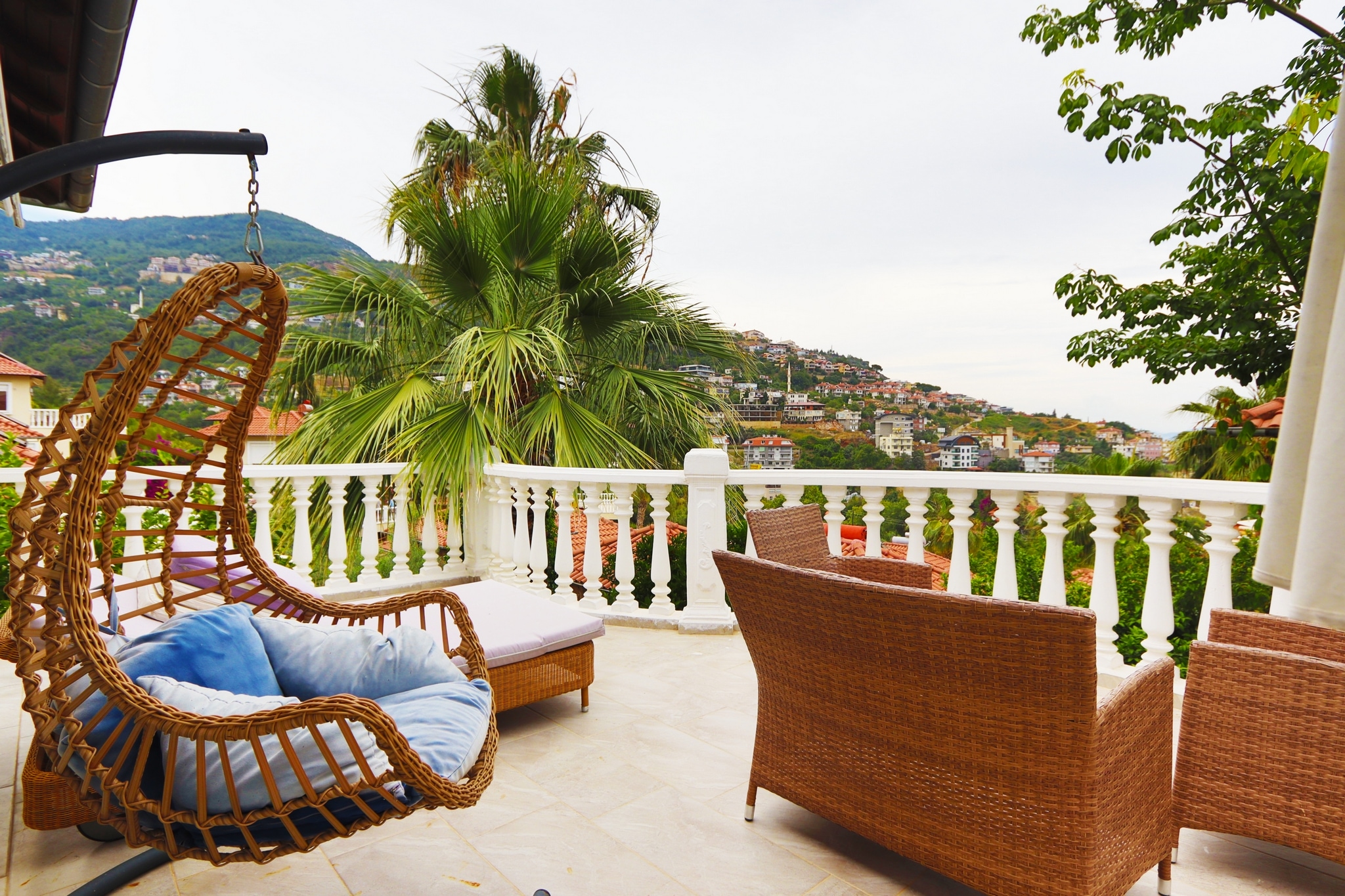Terrace with a hanging wicker chair, wicker sofa and white balustrade in Alanya