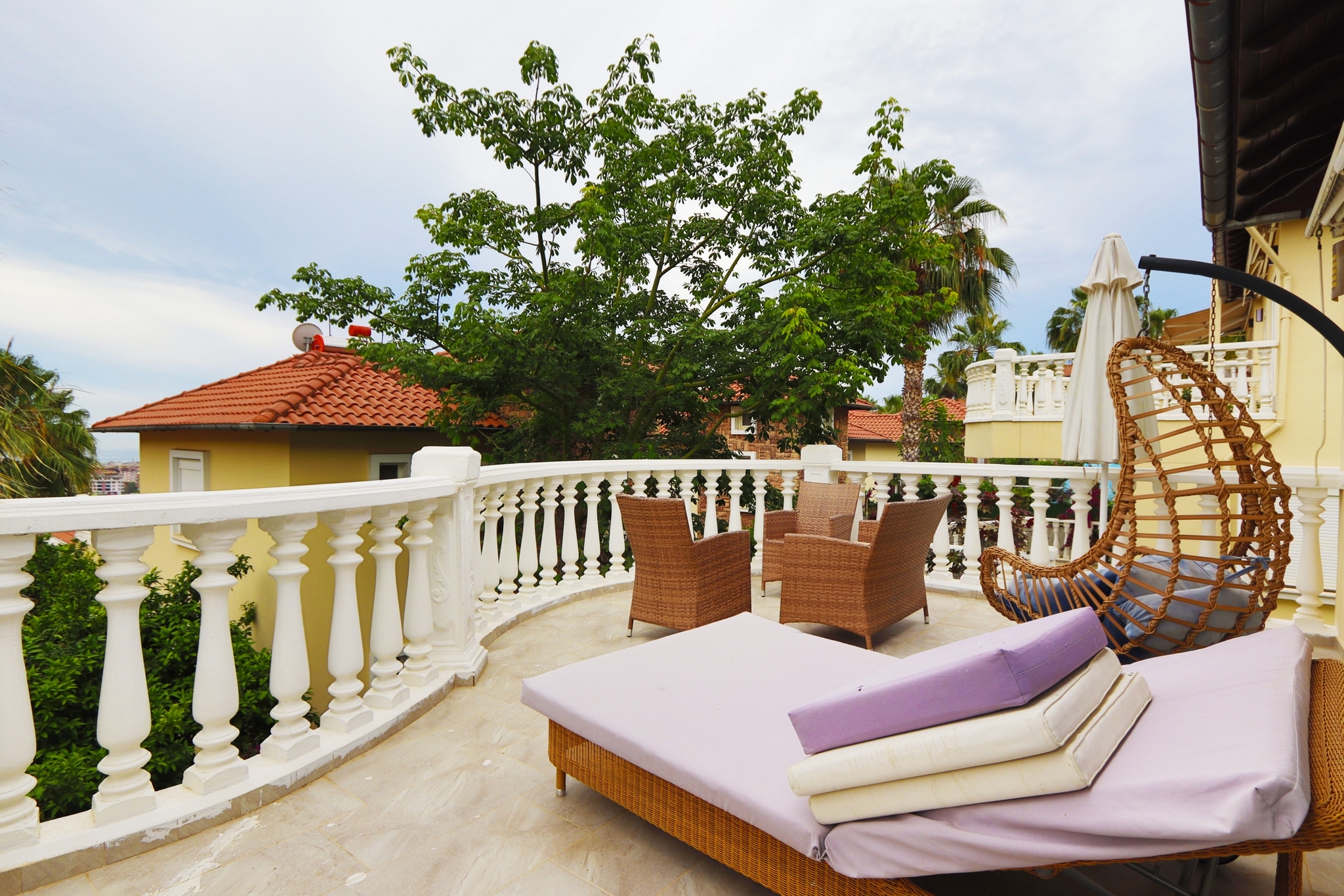 Terrace with a wicker lounger, hanging chair and white balustrade at a villa for sale in Turkey