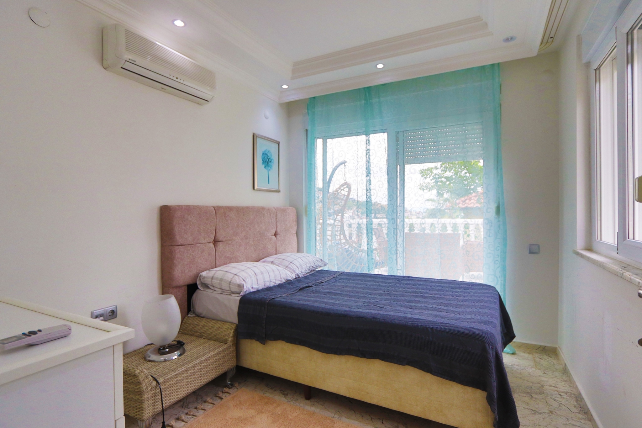 Bedroom with a single bed, dark blue coverlet and turquoise curtains beside a balcony door
