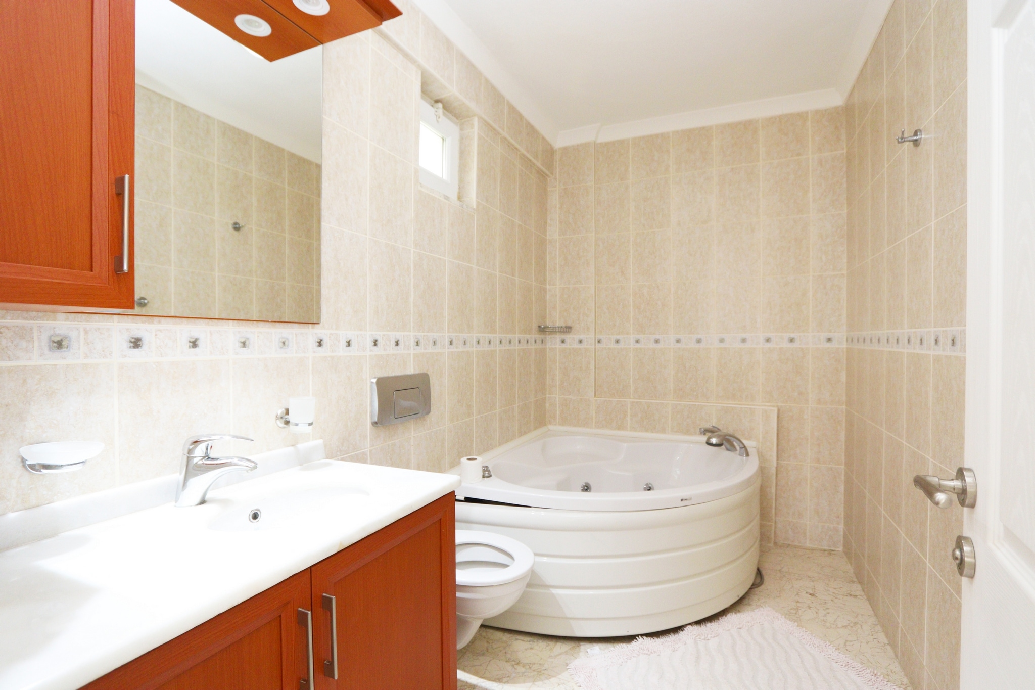 Bathroom with a corner whirlpool tub, vanity and beige wall tiles in a house