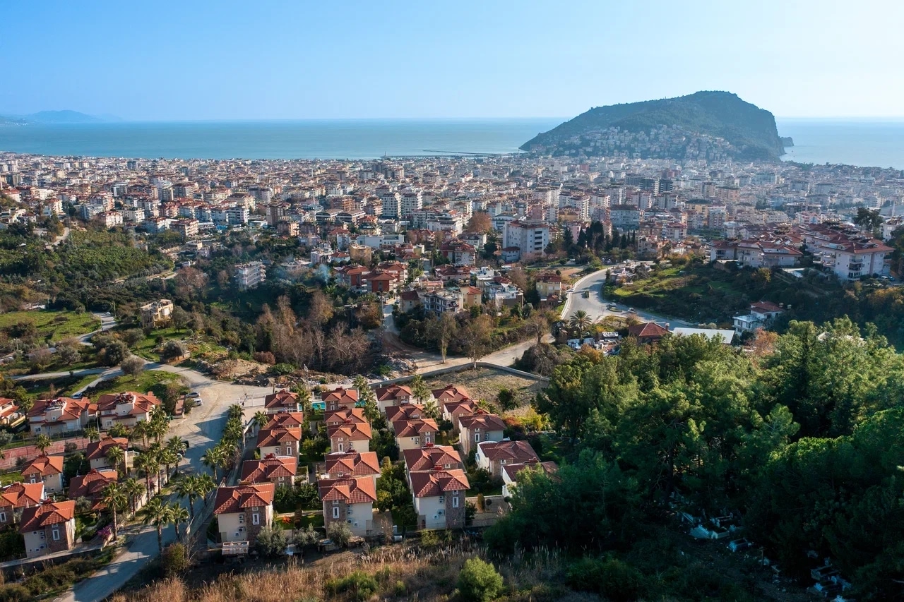 Panoramic city view with a sea bay and green hills, showing a villa for sale in Alanya