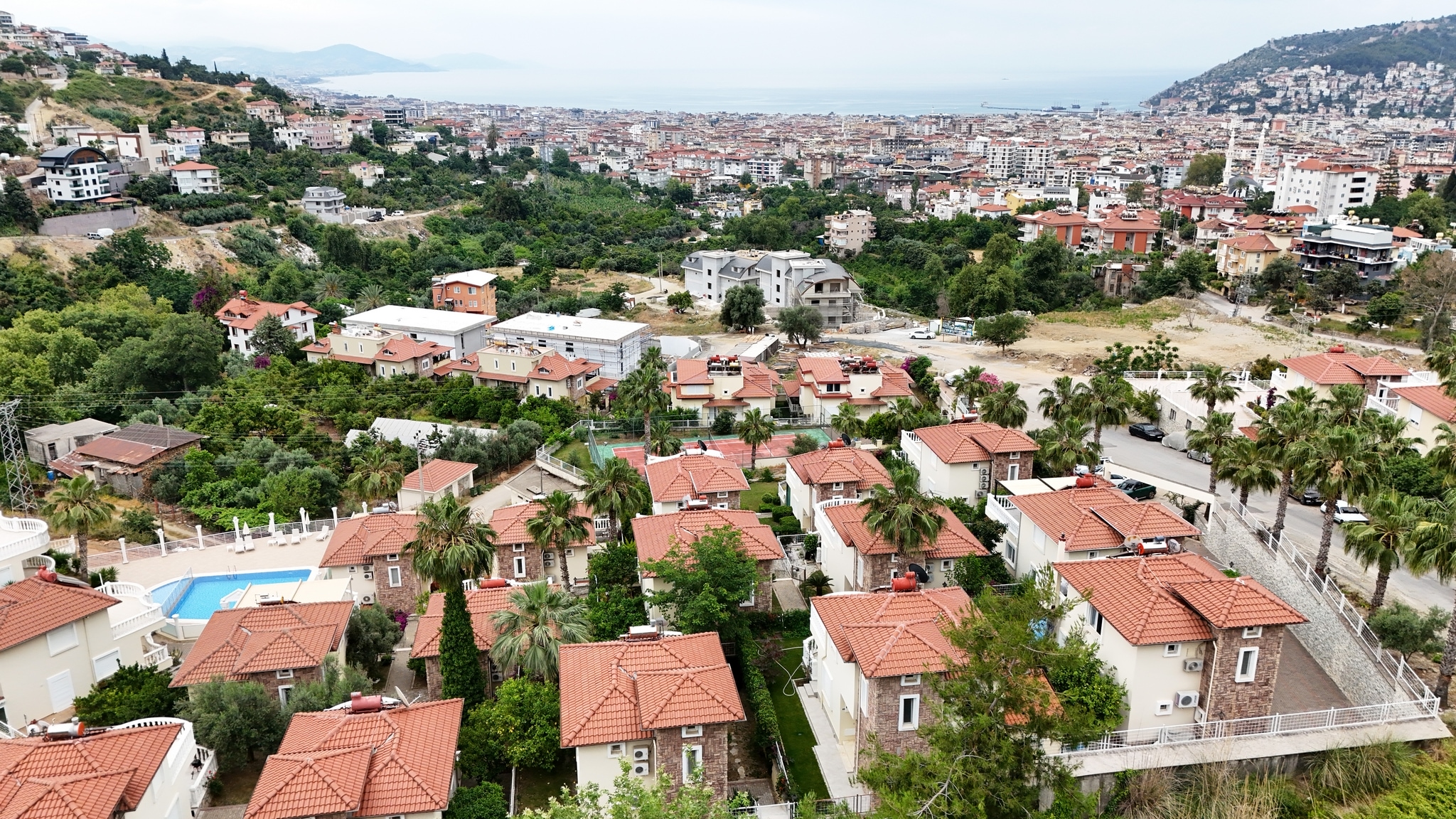 City panorama with a sea bay, palms and a pool among homes, showing a villa for sale in Turkey