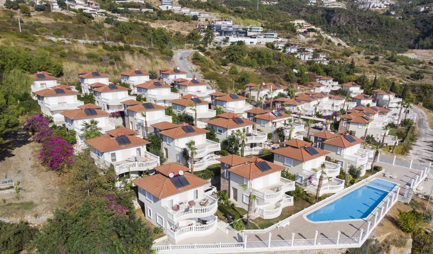 Outdoor pool with white villas and palms in a complex with houses on a mountain slope in Alanya