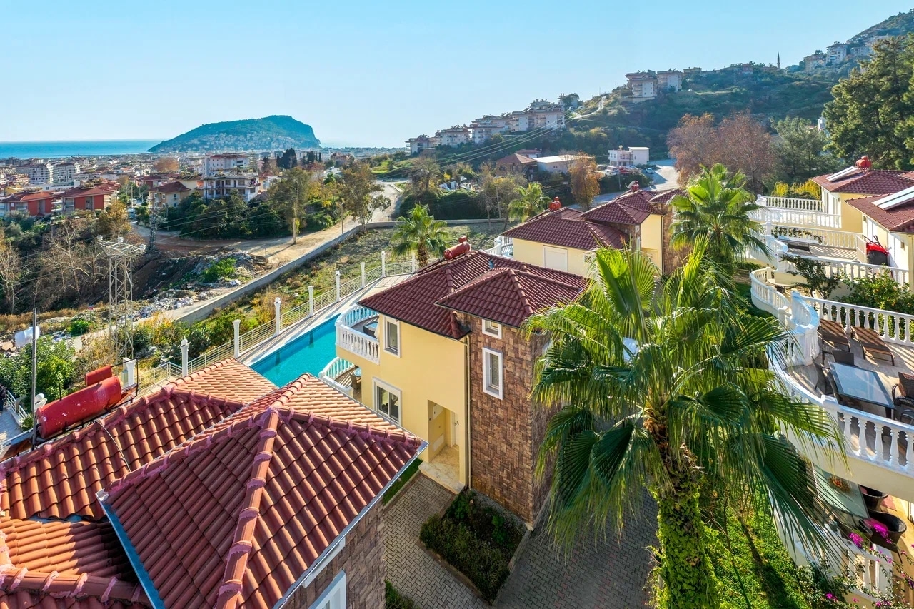 Elevated view of a villa complex with a pool, palms, hills and sea on the horizon in Alanya, Turkey